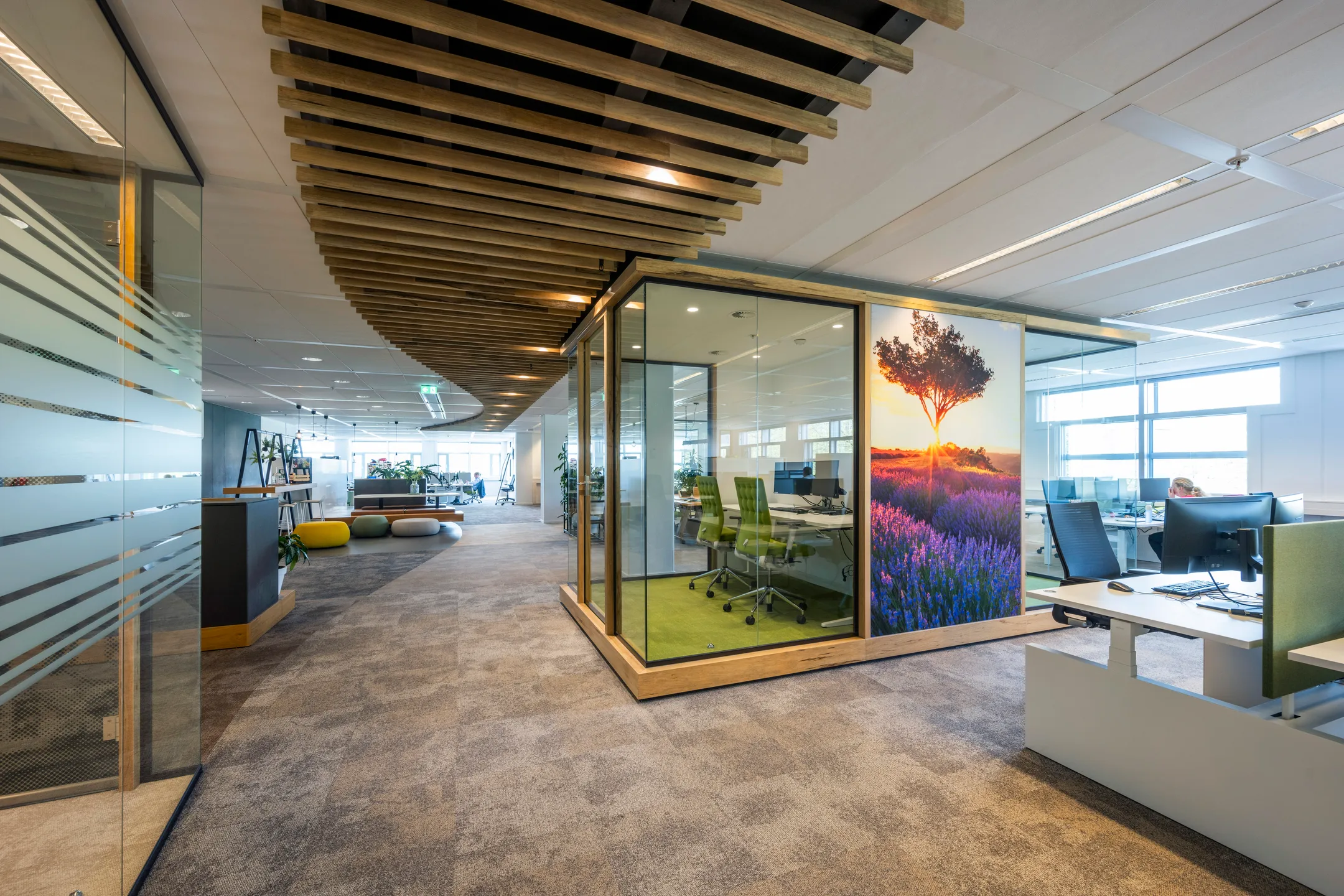 Een modern kantoorinterieur met glazen wanden, opvallende plafondafwerking en bureaus.