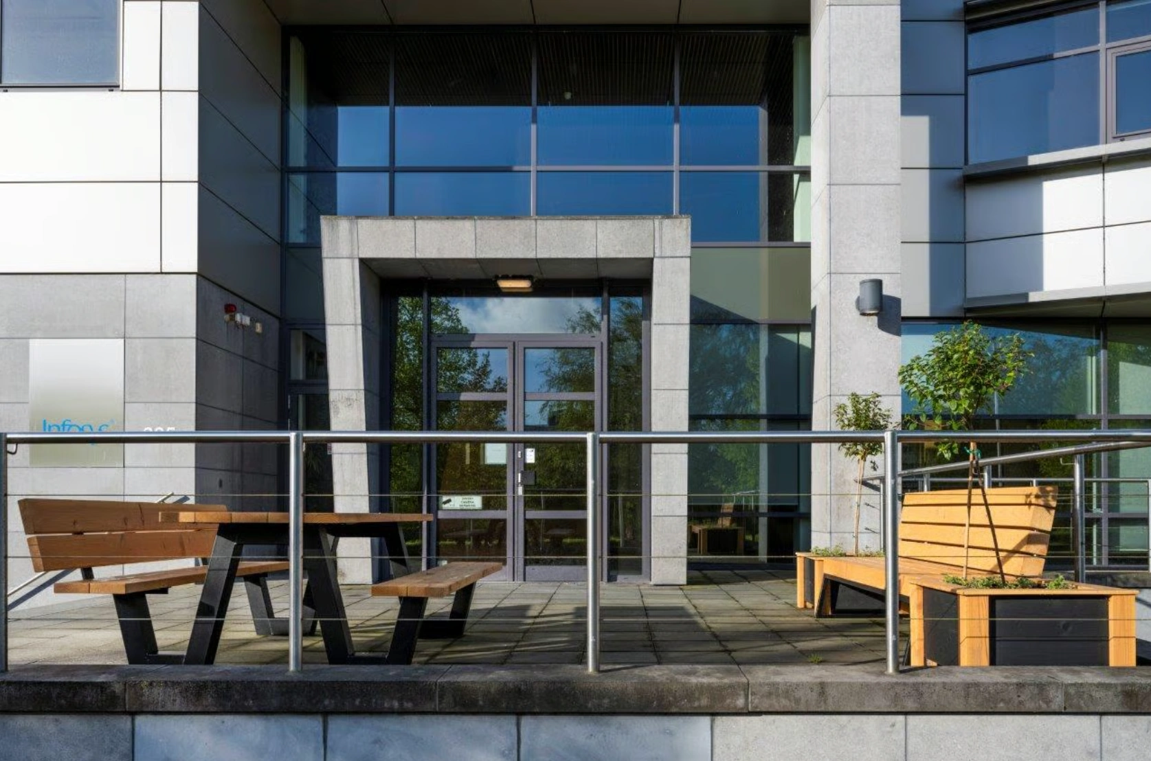 Ingang van een modern kantoorpand aan de Boeing Avenue met houten zitbanken en planten op het terras.