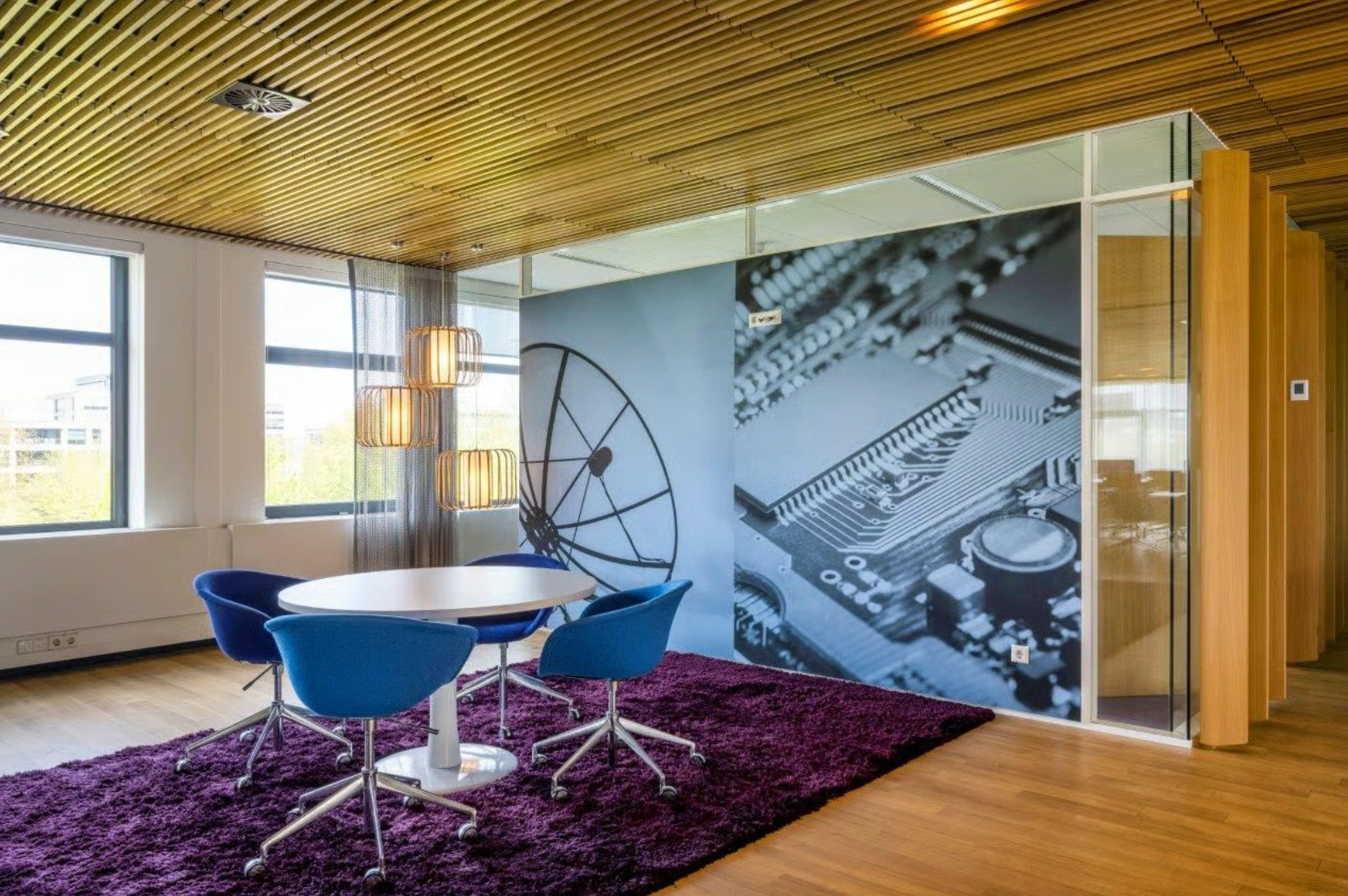 Kleine vergaderruimte op Boeing Avenue met moderne inrichting, blauwe stoelen, paarse vloerbedekking en een muurprint van een satellietschotel en printplaat.