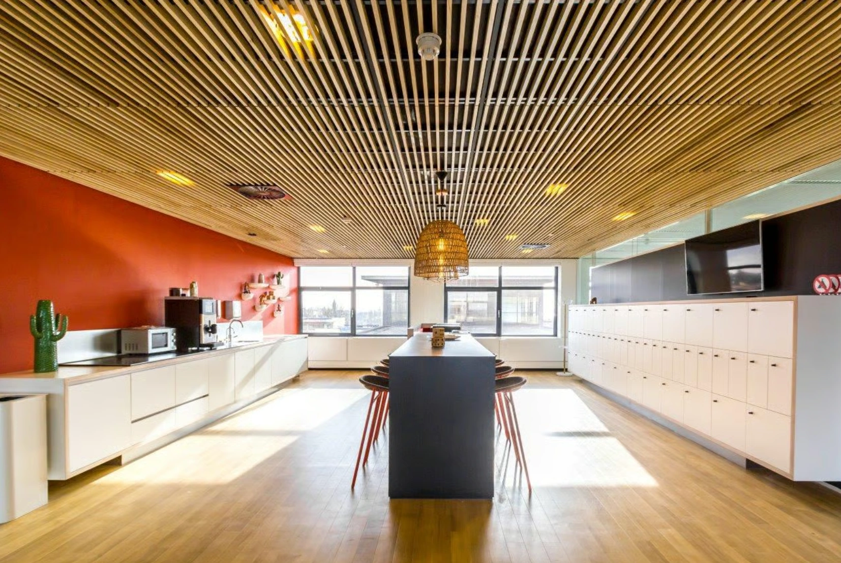 Moderne kantoorkeuken aan de Boeing Avenue met een lange eettafel, rode accentmuur en plafond met houten latten.
