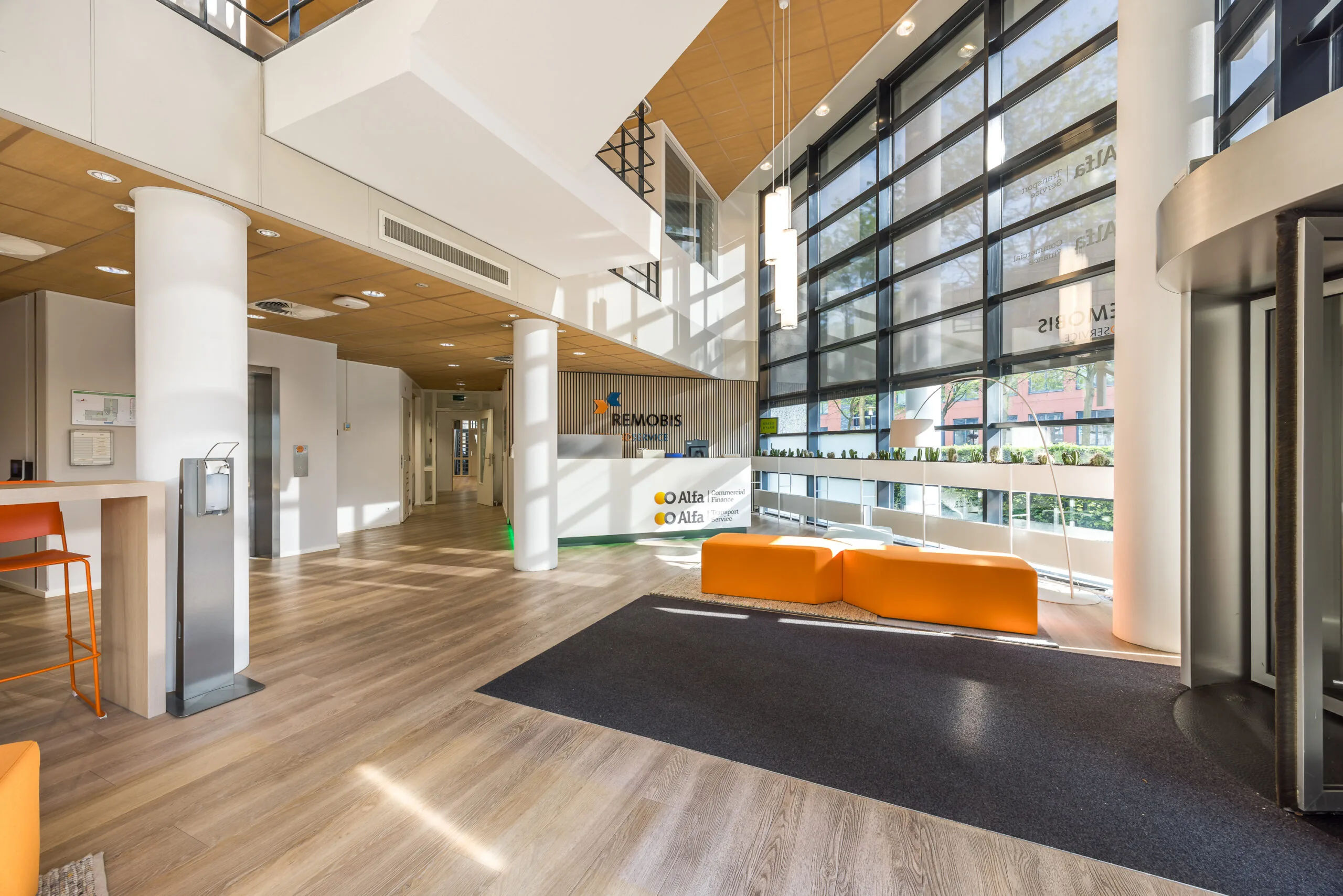 Moderne en lichte entreehal van kantoorgebouw aan de Varrolaan, met oranje zitbanken en balie van REMOBIS en Alfa.