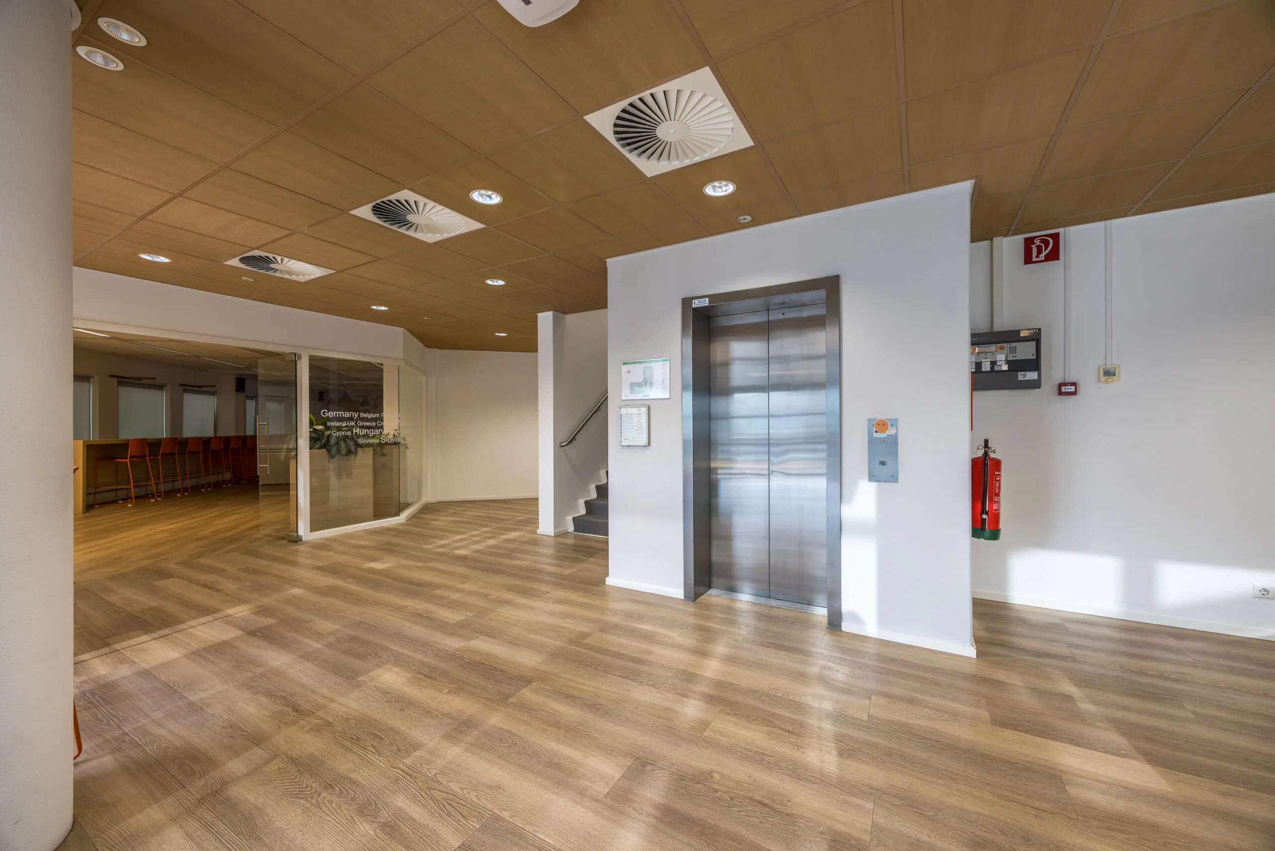 Moderne en nette kantoorlobby aan de Varrolaan met houten vloer, glazen vergaderruimte en een roestvrijstalen lift.