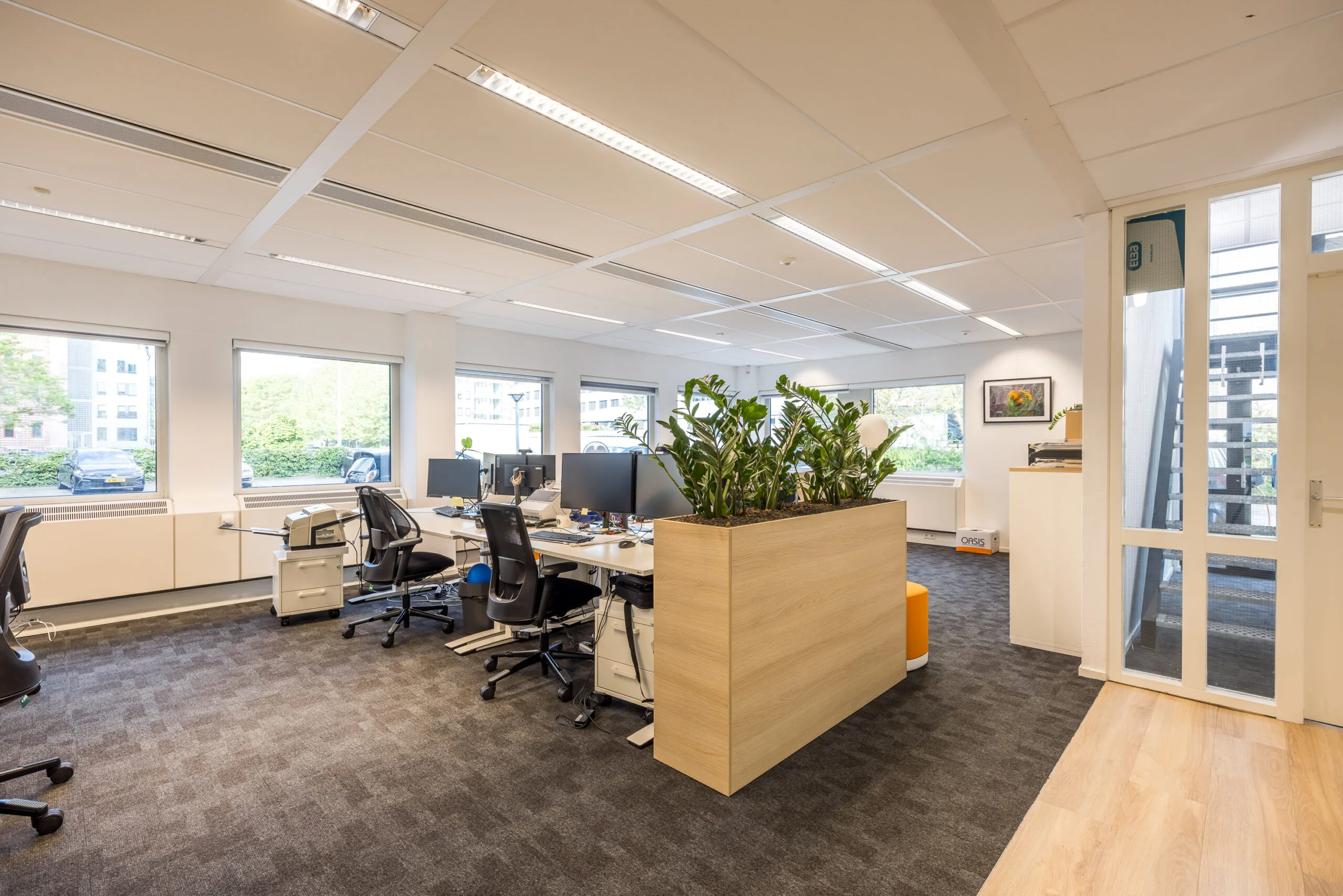 Modern en licht kantoor aan de Varrolaan met flexwerkplekken, grote ramen en een plantenbak als ruimteverdeler.