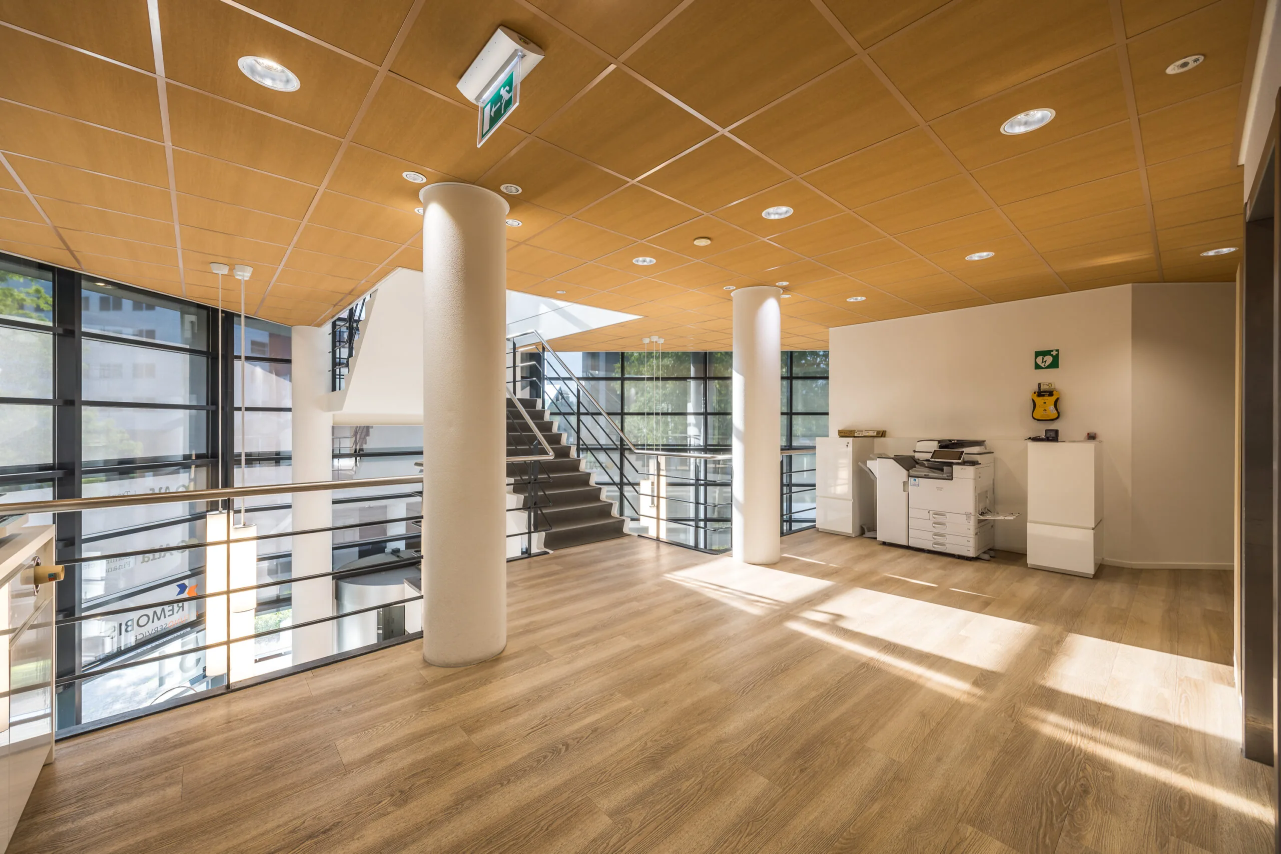 Moderne, lichte kantoorruimte aan de Varrolaan met houten vloer, glazen balustrade en een trap naar beneden.