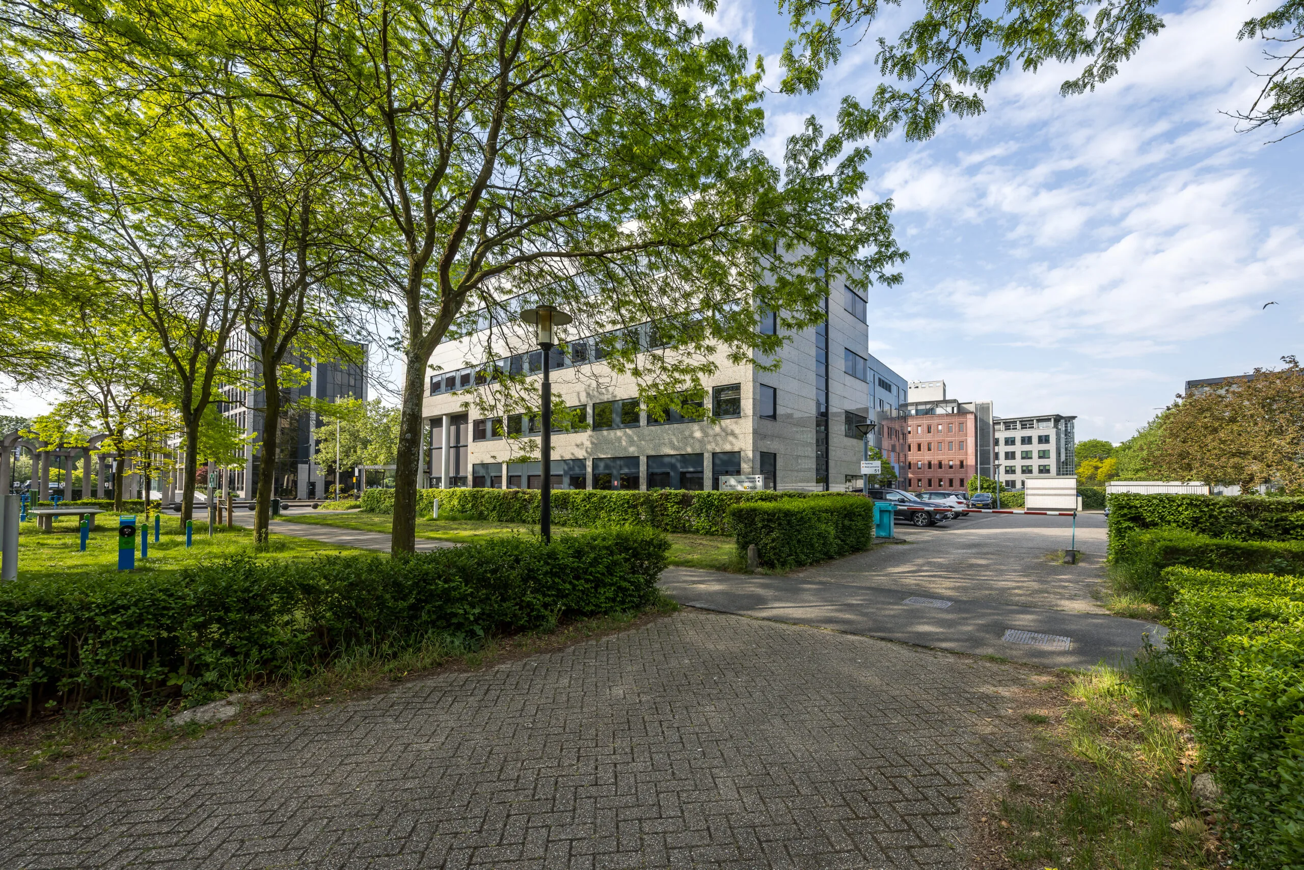 Kantoorgebouw aan de Varrolaan in een groene, stedelijke omgeving met bomen en geparkeerde auto's.