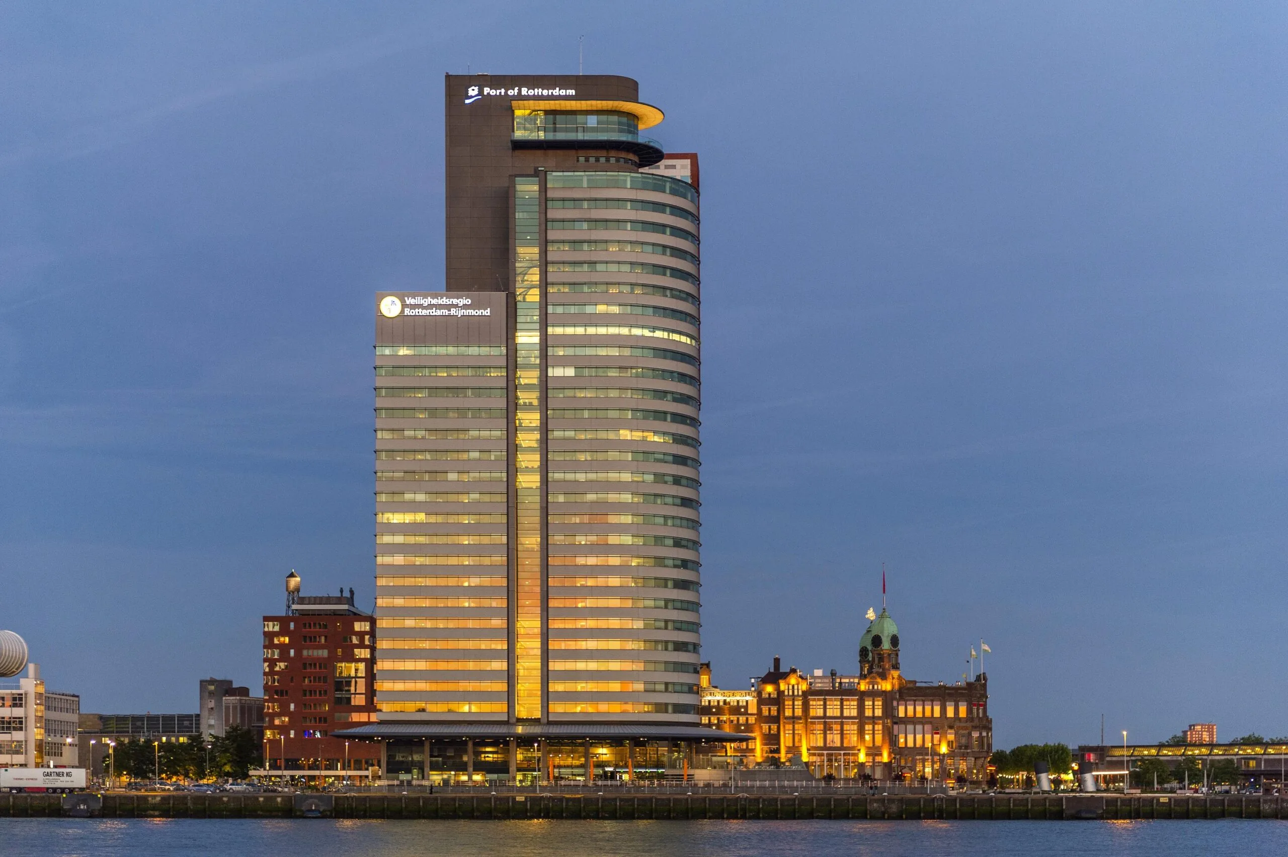 Verlichte kantoorgebouwen aan de Wilhelminakade in Rotterdam, met prominent het gebouw van Port of Rotterdam.