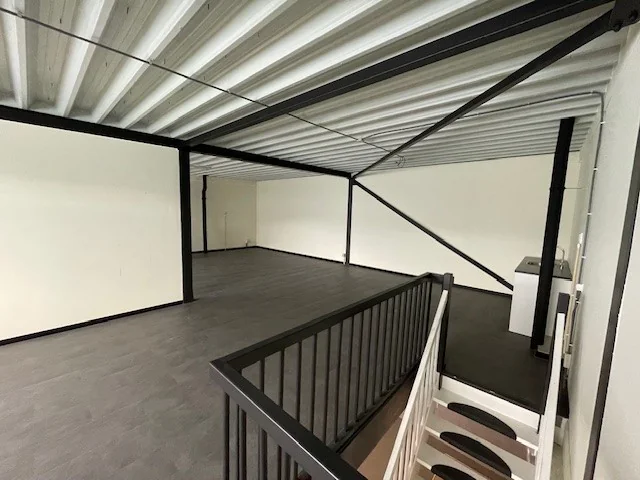 Een lege, industriële bovenverdieping met metalen plafond, donkere vloer en witte trap aan de Laan van S'Gravenmade.