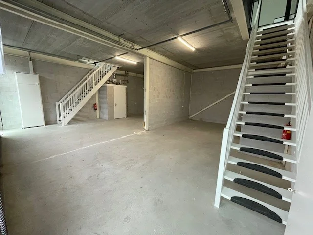 Interieur van een lege bedrijfshal aan de Laan van ’s-Gravenmade met betonnen vloer, twee witte trappen en een technische installatie.