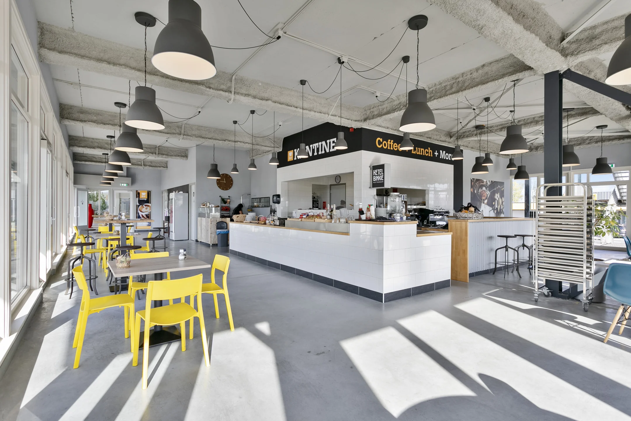 Moderne en lichte bedrijfskantine aan de Hoefsmidstraat met gele stoelen, industriële verlichting en een koffie- en lunchcounter.