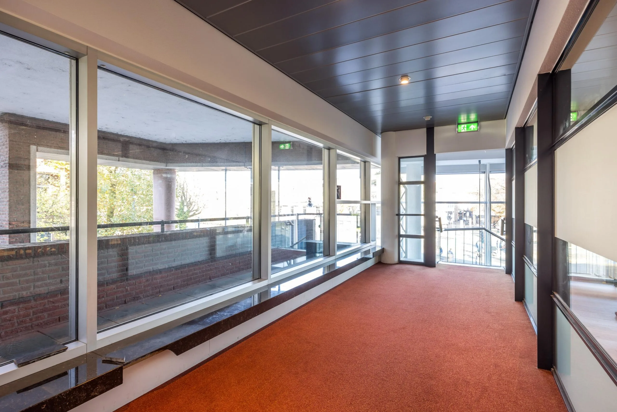 Geverfde gang met rood tapijt, grote ramen en een uitzicht op het balkon aan de Arnhemseweg.