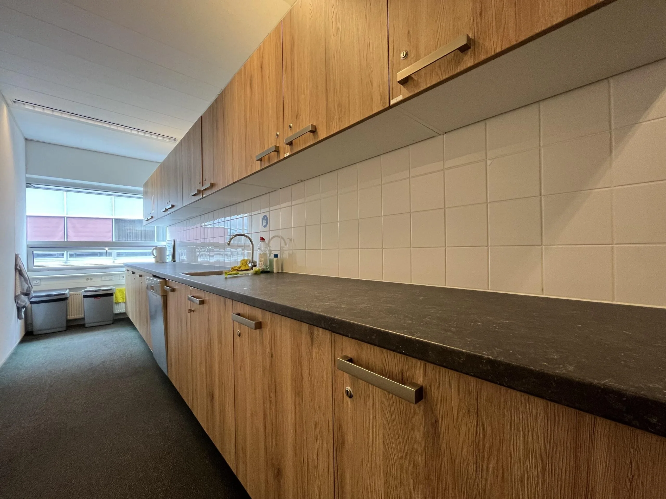 Keuken met houten kastjes en zwart aanrechtblad in een kantoor aan de Arnhemseweg.