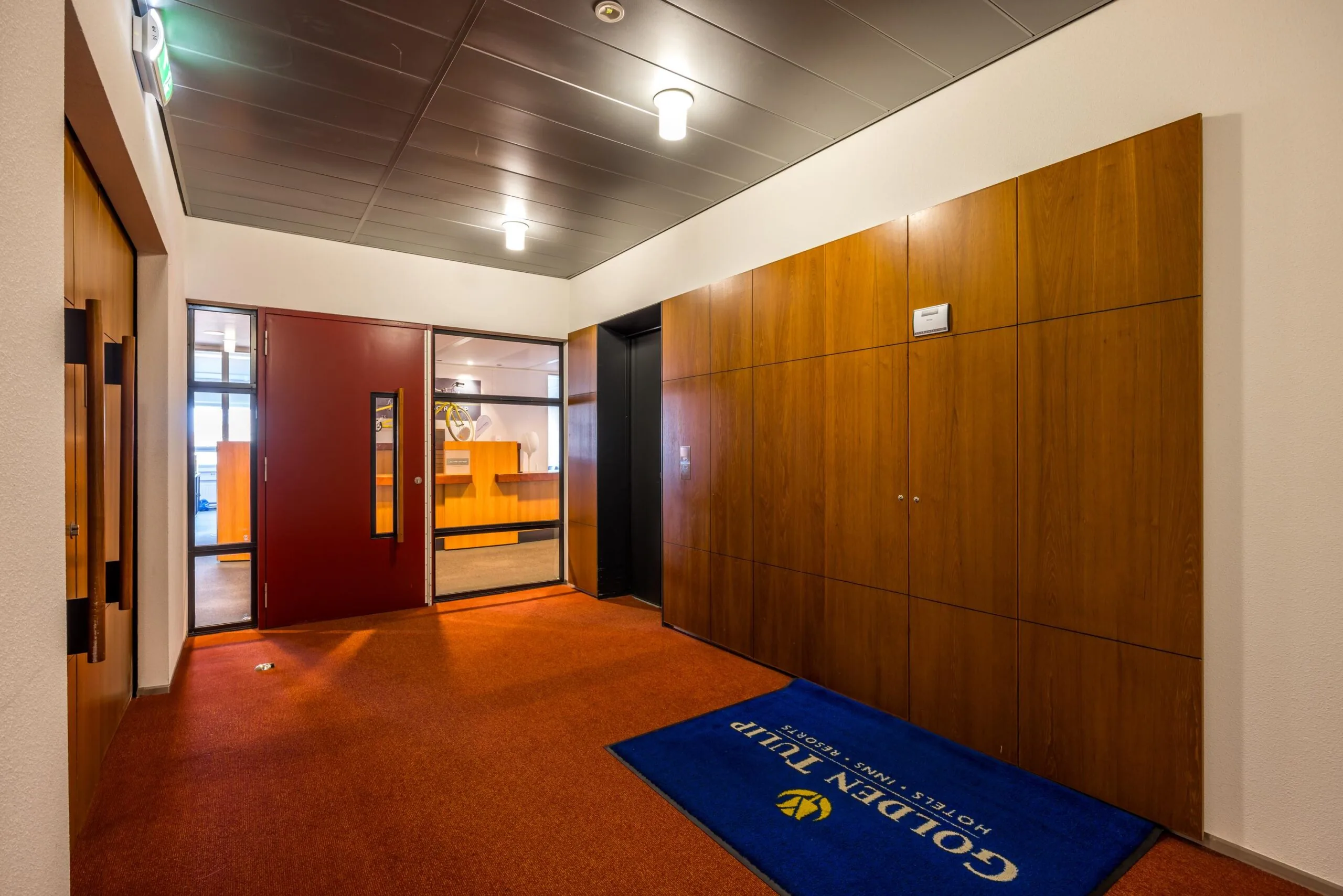 Entreehal van Golden Tulip aan de Arnhemseweg met rode vloerbedekking, houten wandpanelen en zicht op de receptie.
