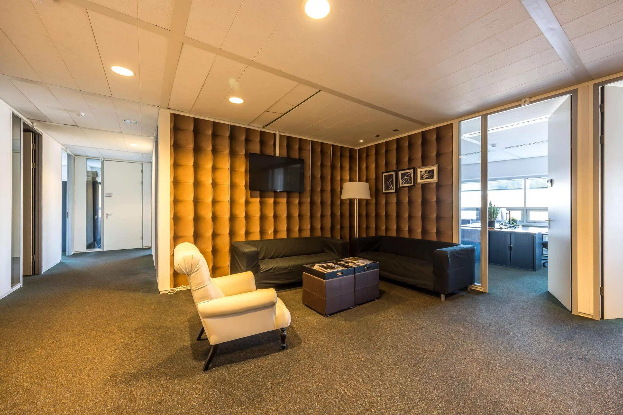 Moderne wachtruimte met leren banken, een tv, en een gecapitonneerde wand in een kantoor aan de Arnhemseweg.