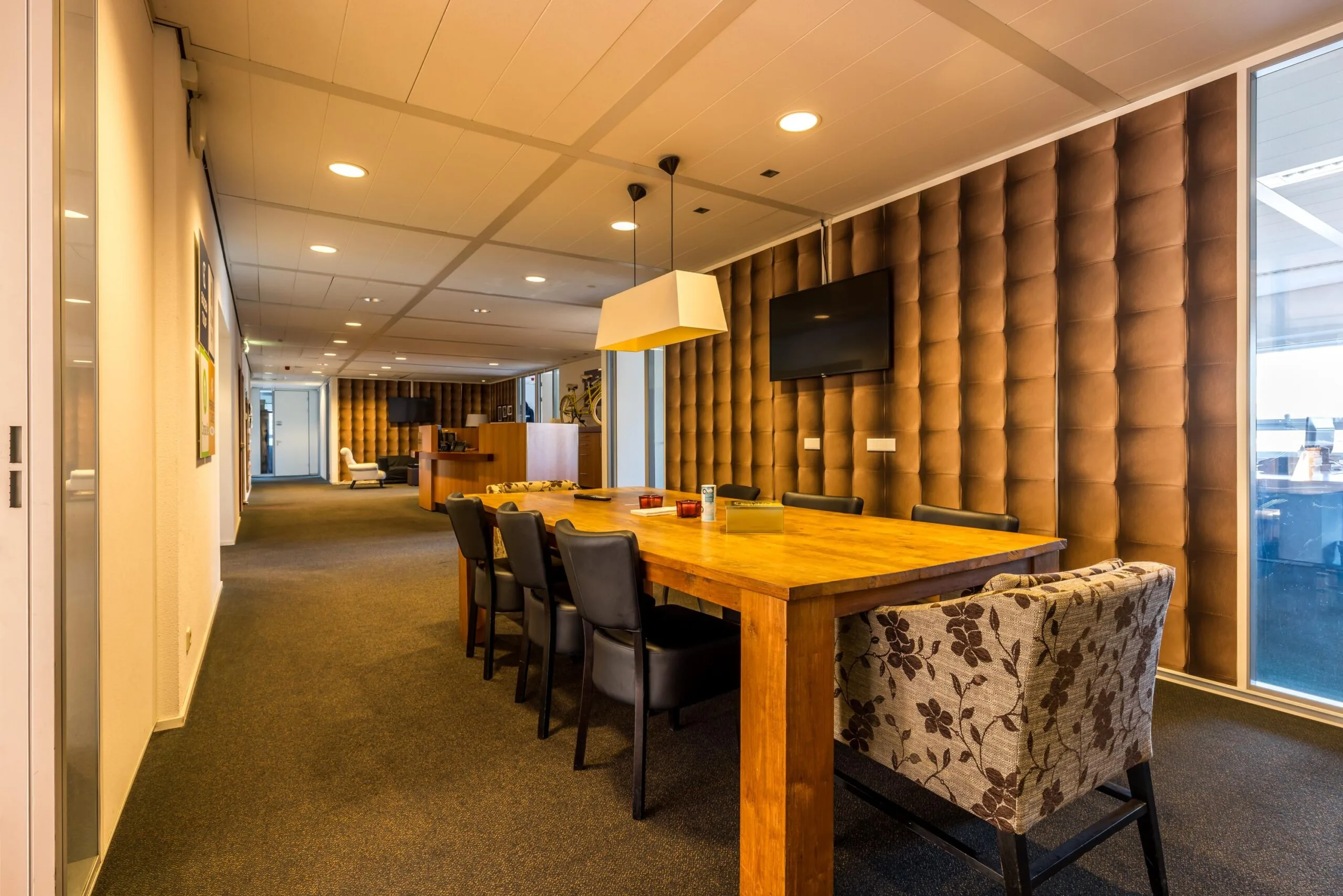 Moderne vergaderruimte aan de Arnhemseweg met een grote houten tafel, leren stoelen en een wand met gewatteerde bekleding.
