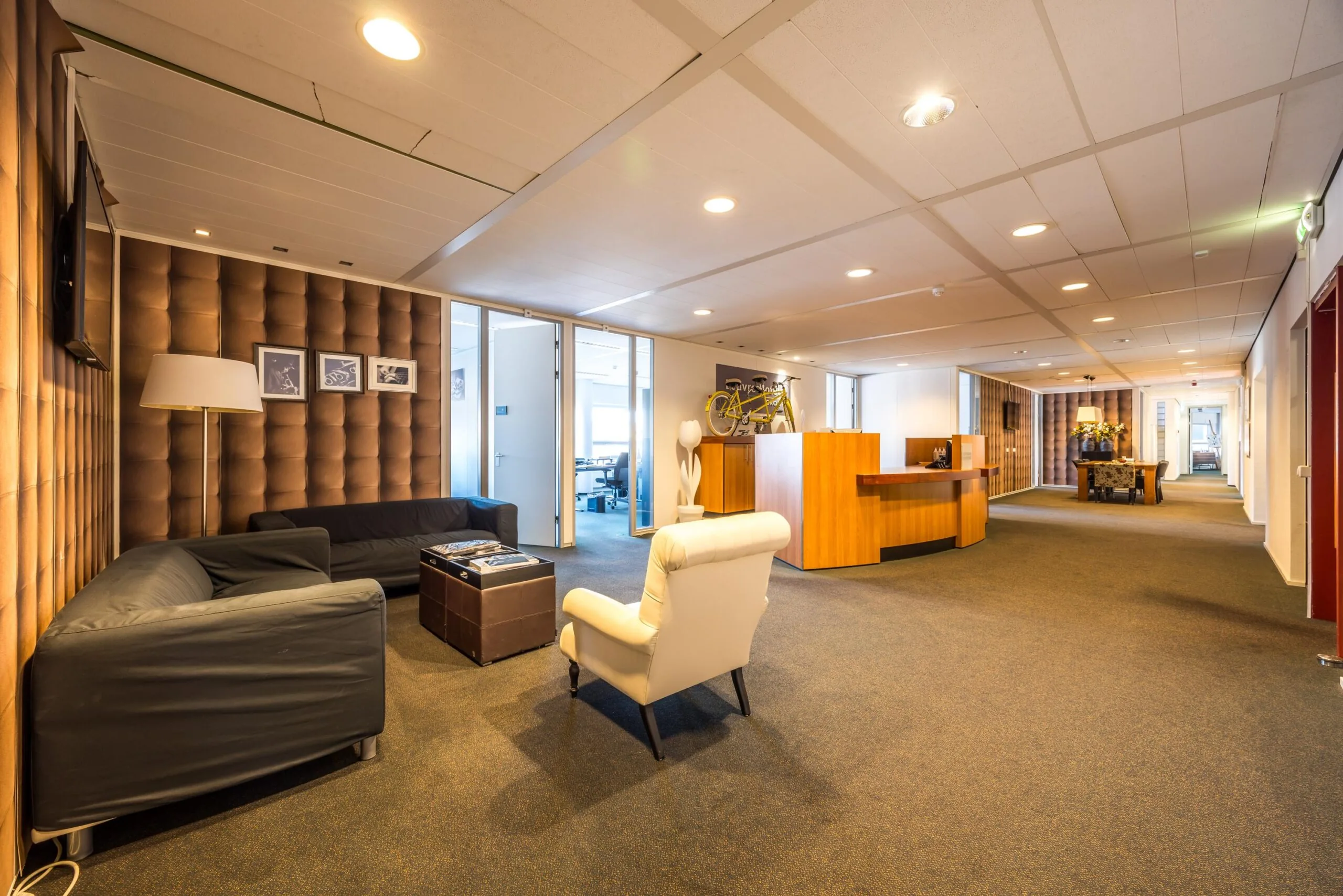Moderne kantoorlobby aan de Arnhemseweg met zithoek, houten balie en decoratieve elementen zoals een gele racefiets en kunst aan de wand.