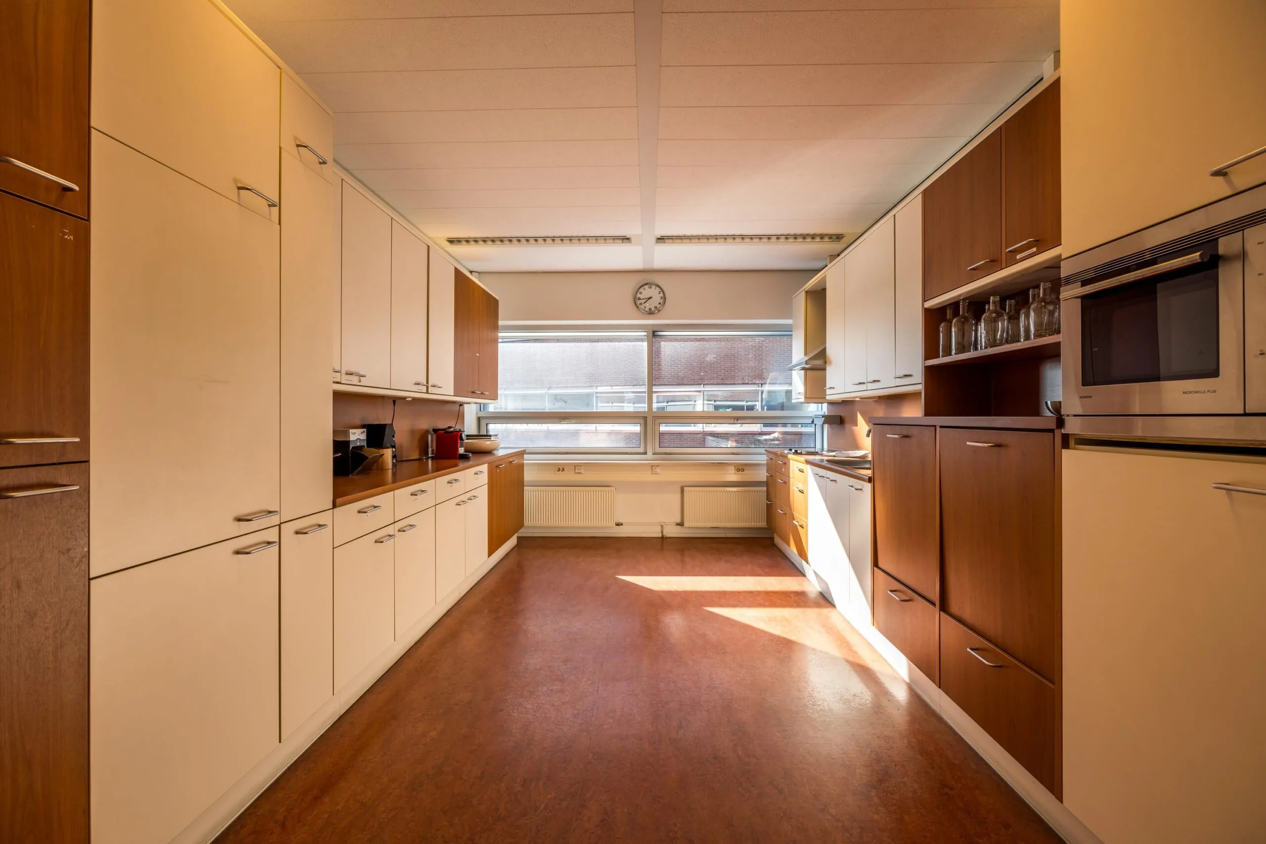 Ruime, symmetrische keuken aan de Arnhemseweg met houten en crèmekleurige kasten, een groot raam en modern inbouwapparatuur.
