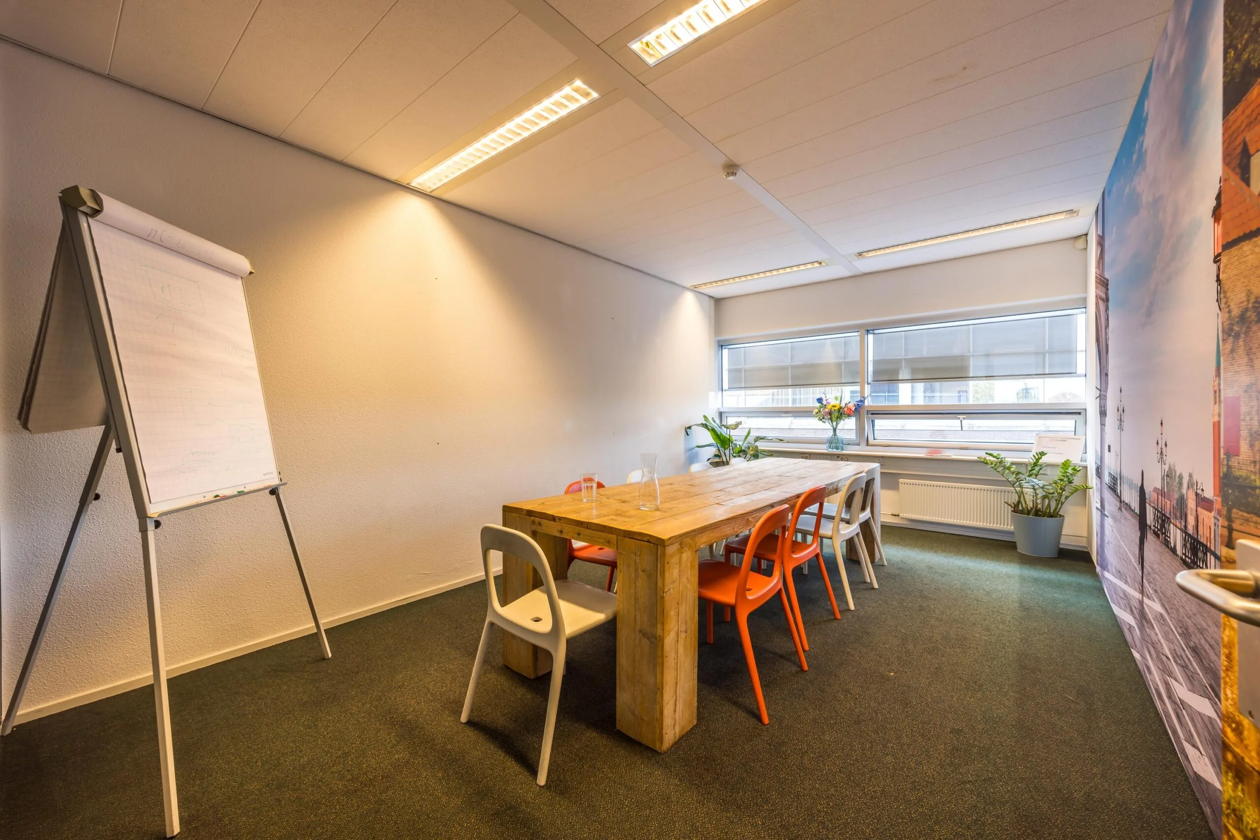 Vergaderruimte aan de Arnhemseweg met houten tafel, gekleurde stoelen, flip-over en grote ramen.