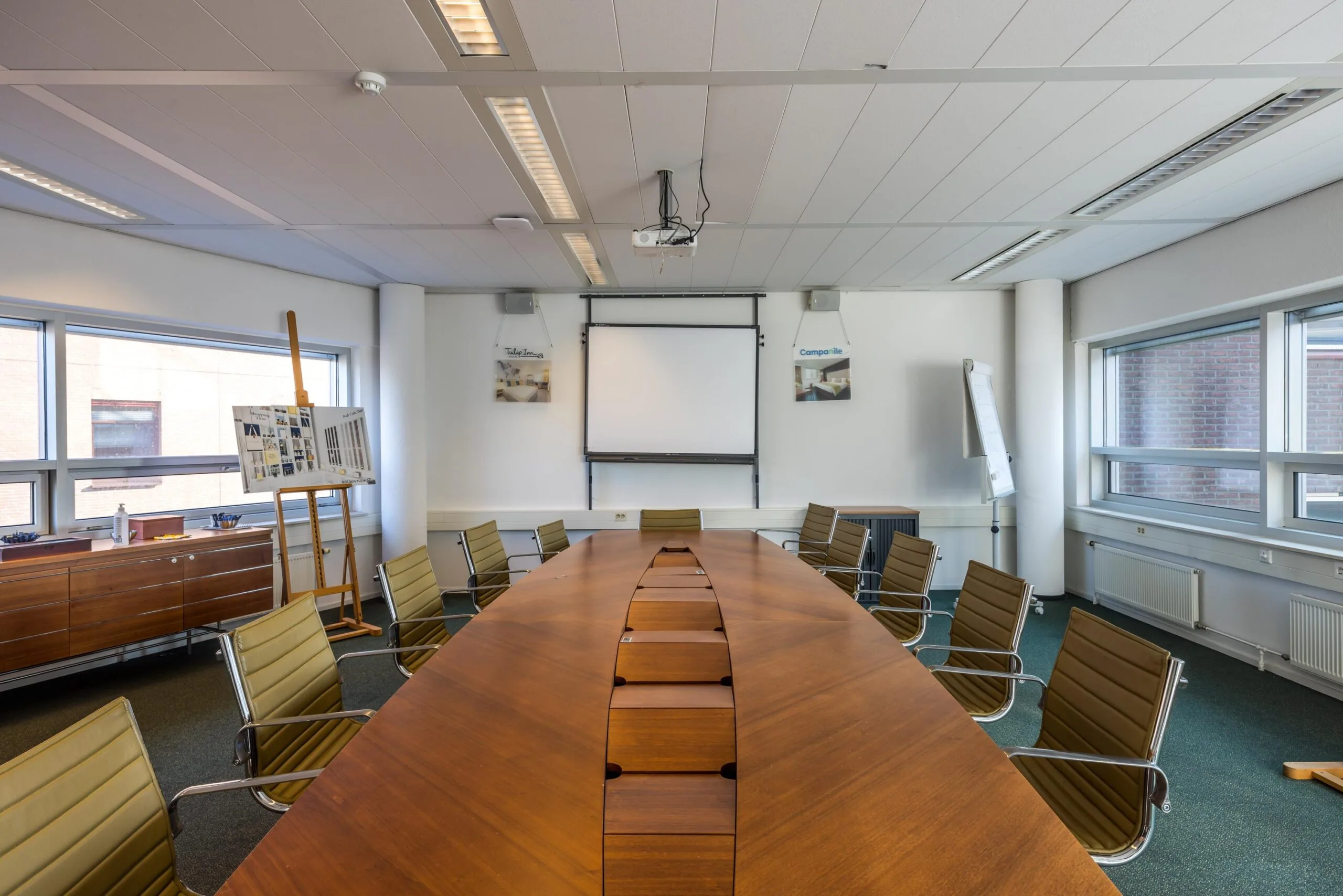 Vergaderruimte aan de Arnhemseweg met groot houten conferentietafel, presentatiebord en projectiescherm.
