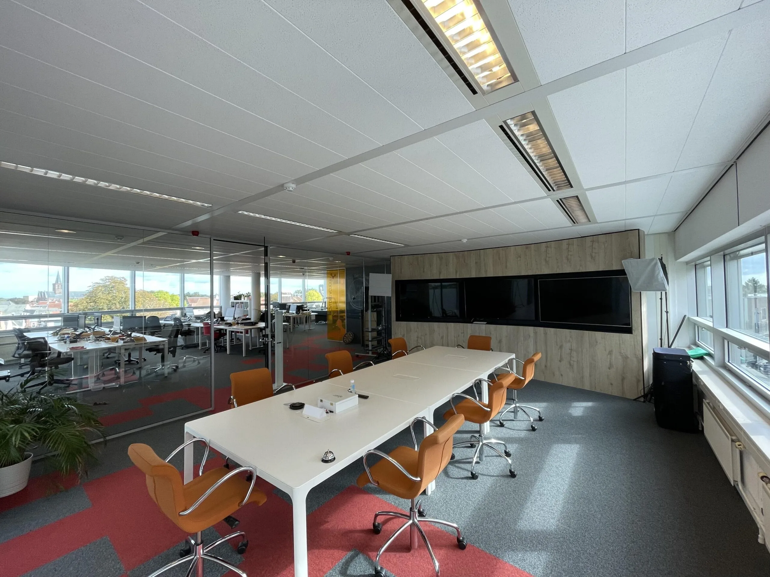Moderne vergaderruimte met oranje stoelen, een lange tafel en grote schermen aan de muur in een kantoor aan de Arnhemseweg.