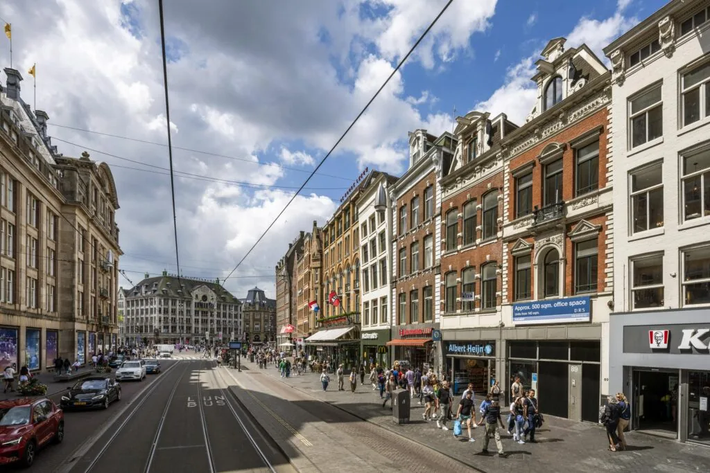 Drukke winkelstraat aan het Damrak in Amsterdam met historische gebouwen, winkels en passerende voetgangers.