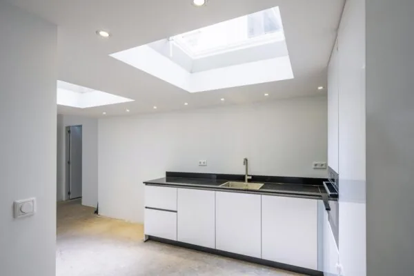 Moderne witte keuken met zwarte accenten en natuurlijke lichtinval via grote dakramen.