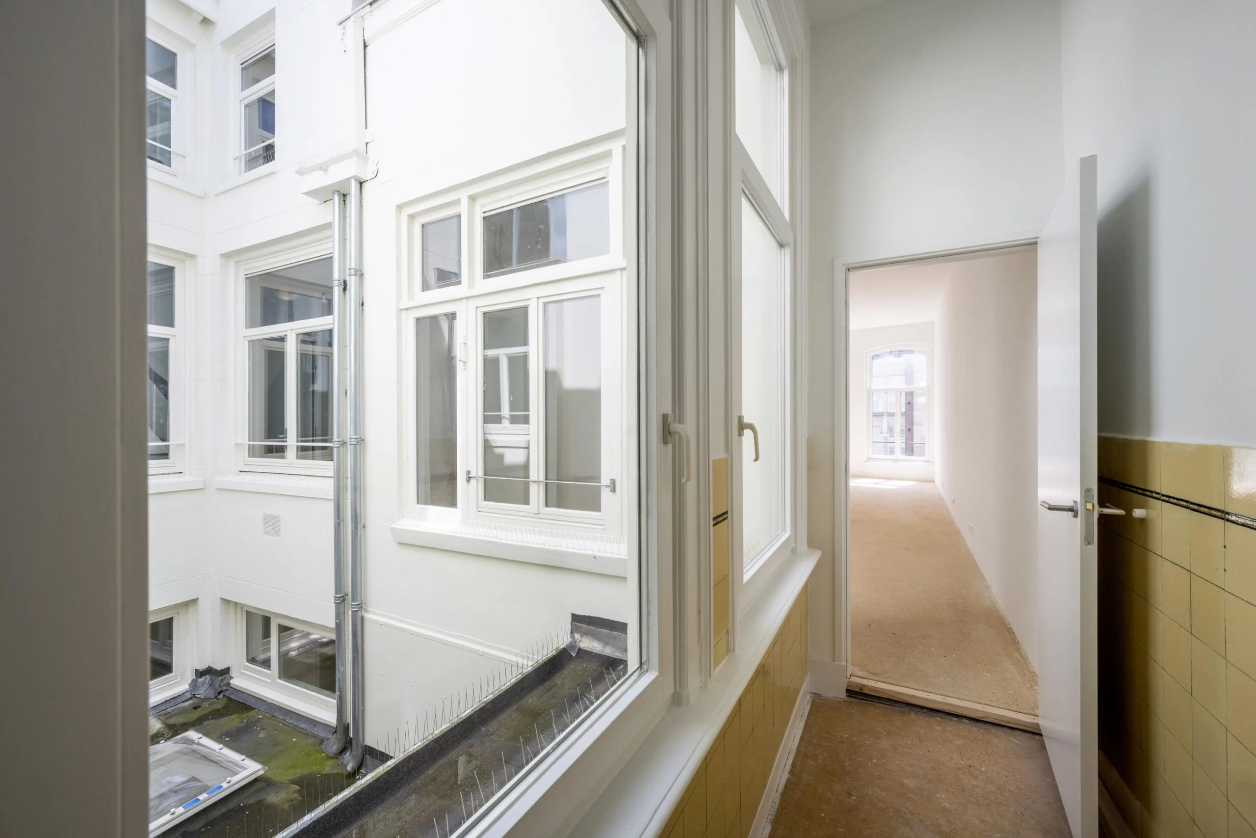 Licht binnenhof met witte gevel en ramen, gezien vanuit een gang met open deur naar een lichte kamer aan het Damrak.
