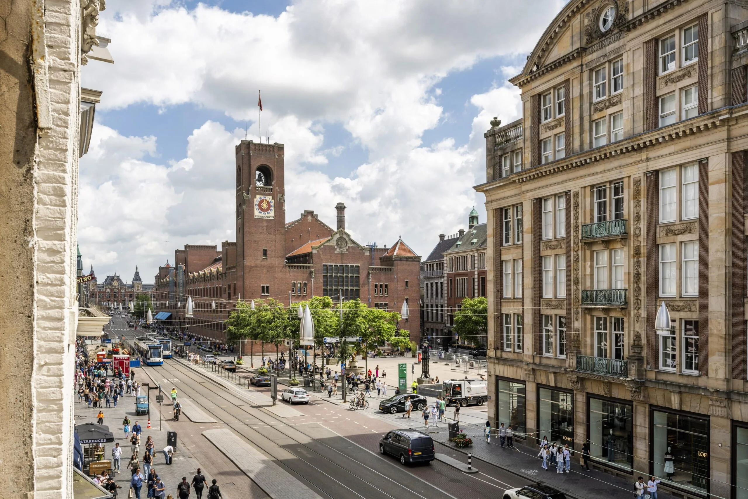 Drukke straat op het Damrak in Amsterdam met zicht op de beurs van Berlage en omliggende historische gebouwen.