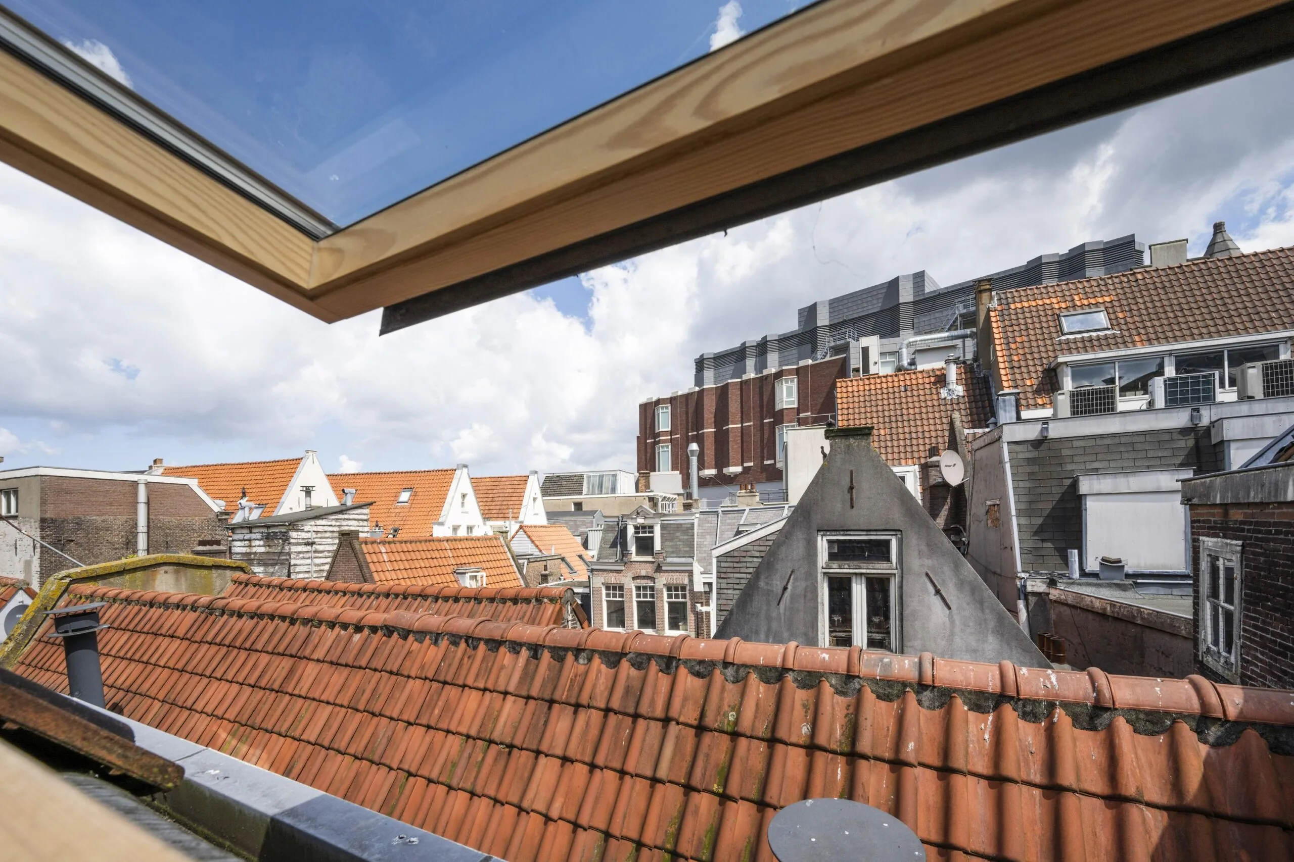 Uitzicht op de daken en gevels van historische panden aan het Damrak in Amsterdam, gezien vanuit een open dakraam.