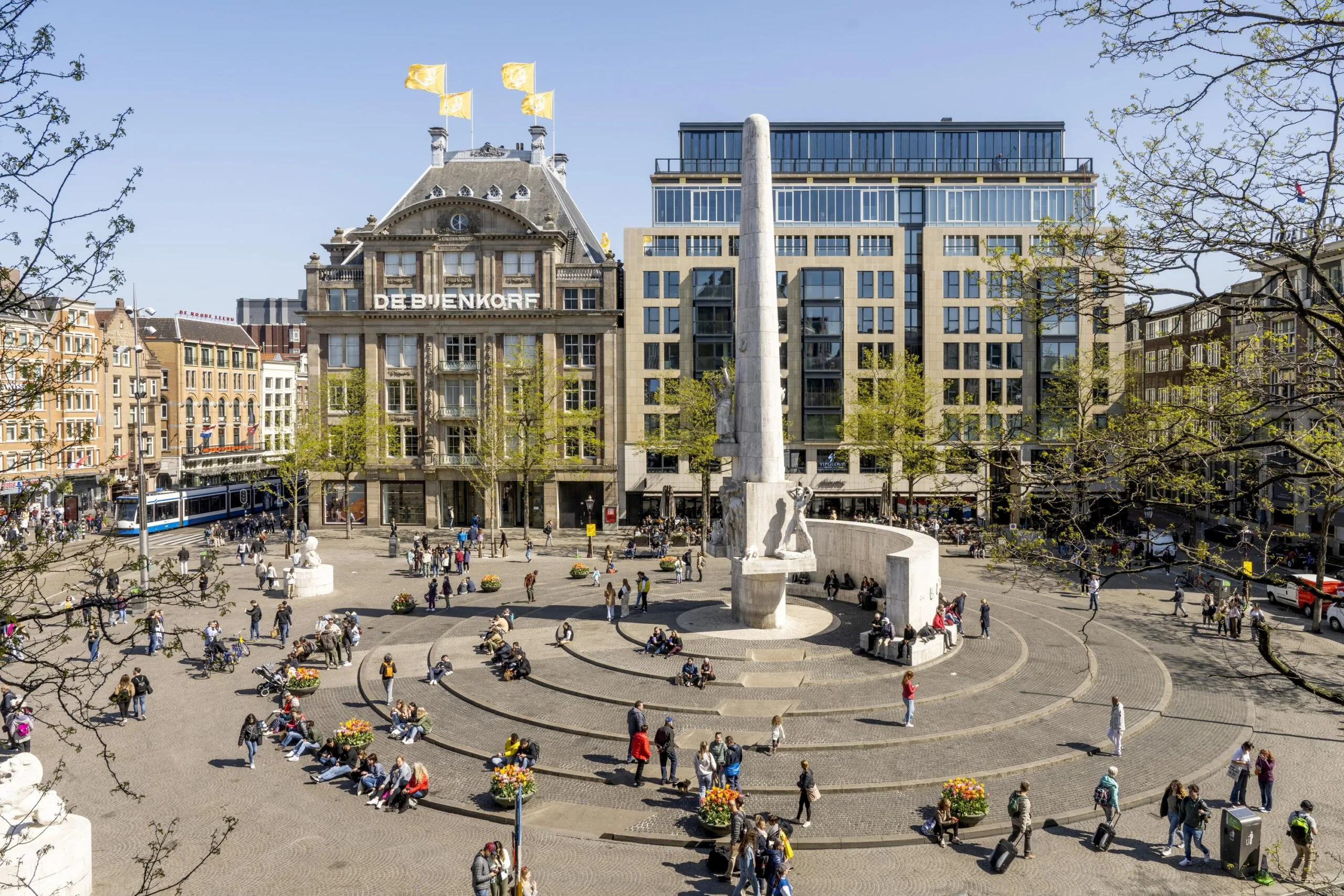 Drukke Dam in Amsterdam met het Nationaal Monument en warenhuis De Bijenkorf op de achtergrond.