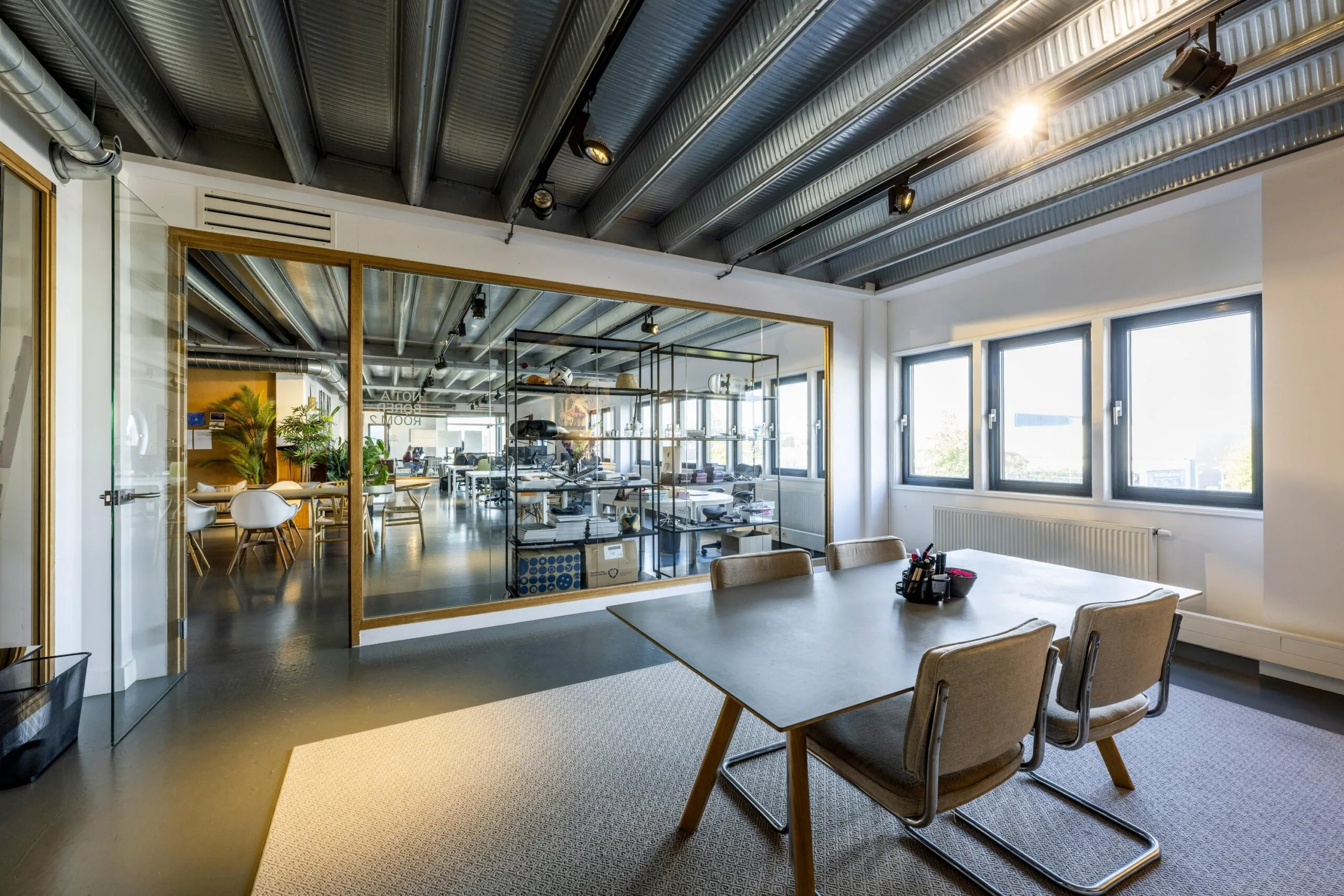 Modern office meeting room with a large table, glass wall, and view into an open workspace on Helicopterstraat.