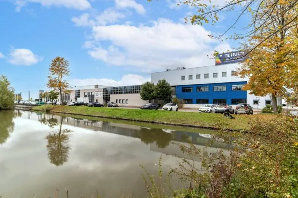 Bedrijfsgebouw aan de Zuiderweg met parkeergelegenheid en een "Te Huur" bord, gelegen aan het water in een herfstlandschap.