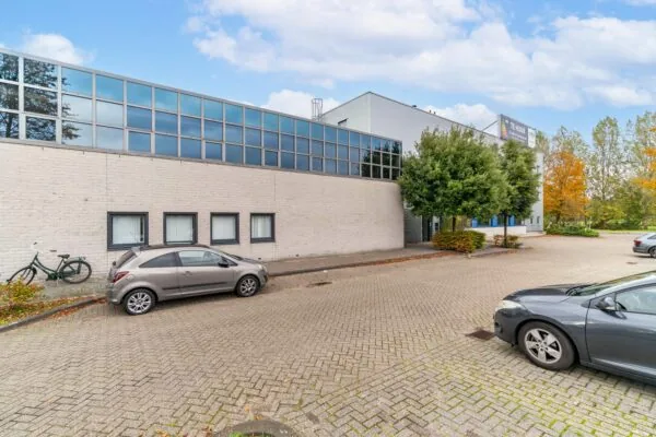 Bedrijfsgebouw aan de Zuiderweg met parkeerplaatsen, geparkeerde auto's en een "Te Huur" bord op de gevel.