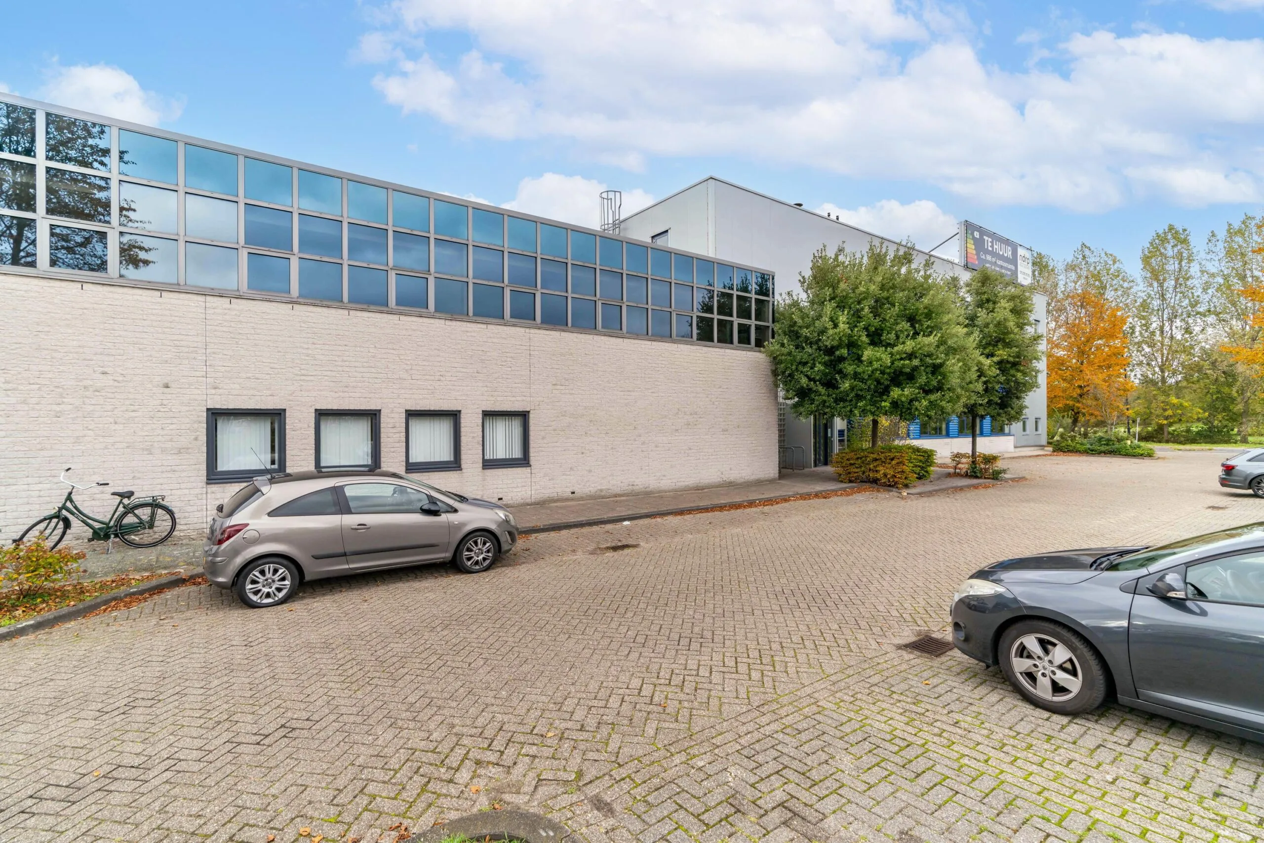 Bedrijfsgebouw aan de Zuiderweg met parkeerplaatsen, geparkeerde auto's en een "Te Huur" bord op de gevel.