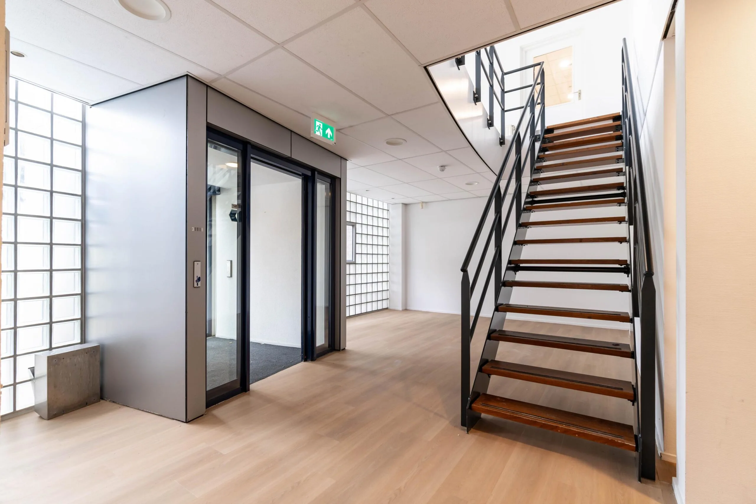 Moderne lichte hal met houten trap en glazen liftdeur aan de Zuiderweg.