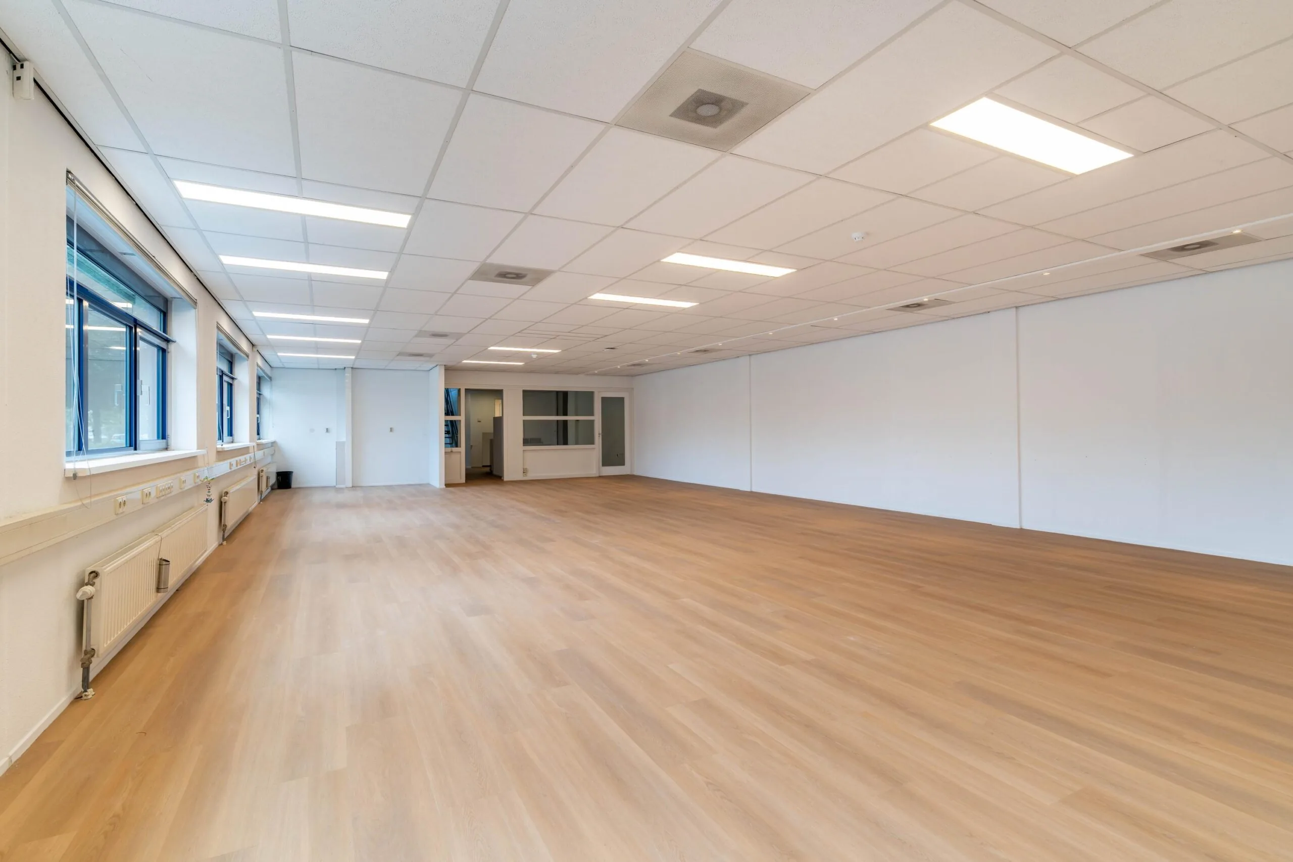 Lichte, lege kantoorruimte aan de Zuiderweg met houten vloer, systeemplafond en grote ramen.