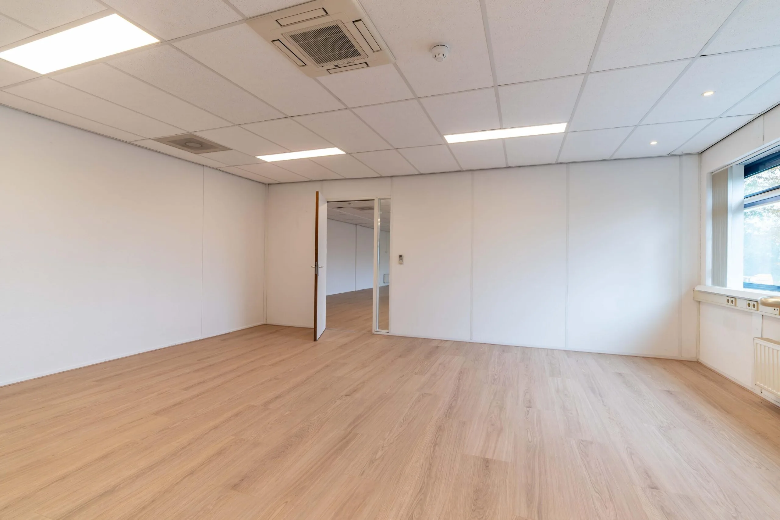Leeg kantoor met houten vloer, systeemplafond en een groot raam aan de rechterzijde op Zuiderweg.