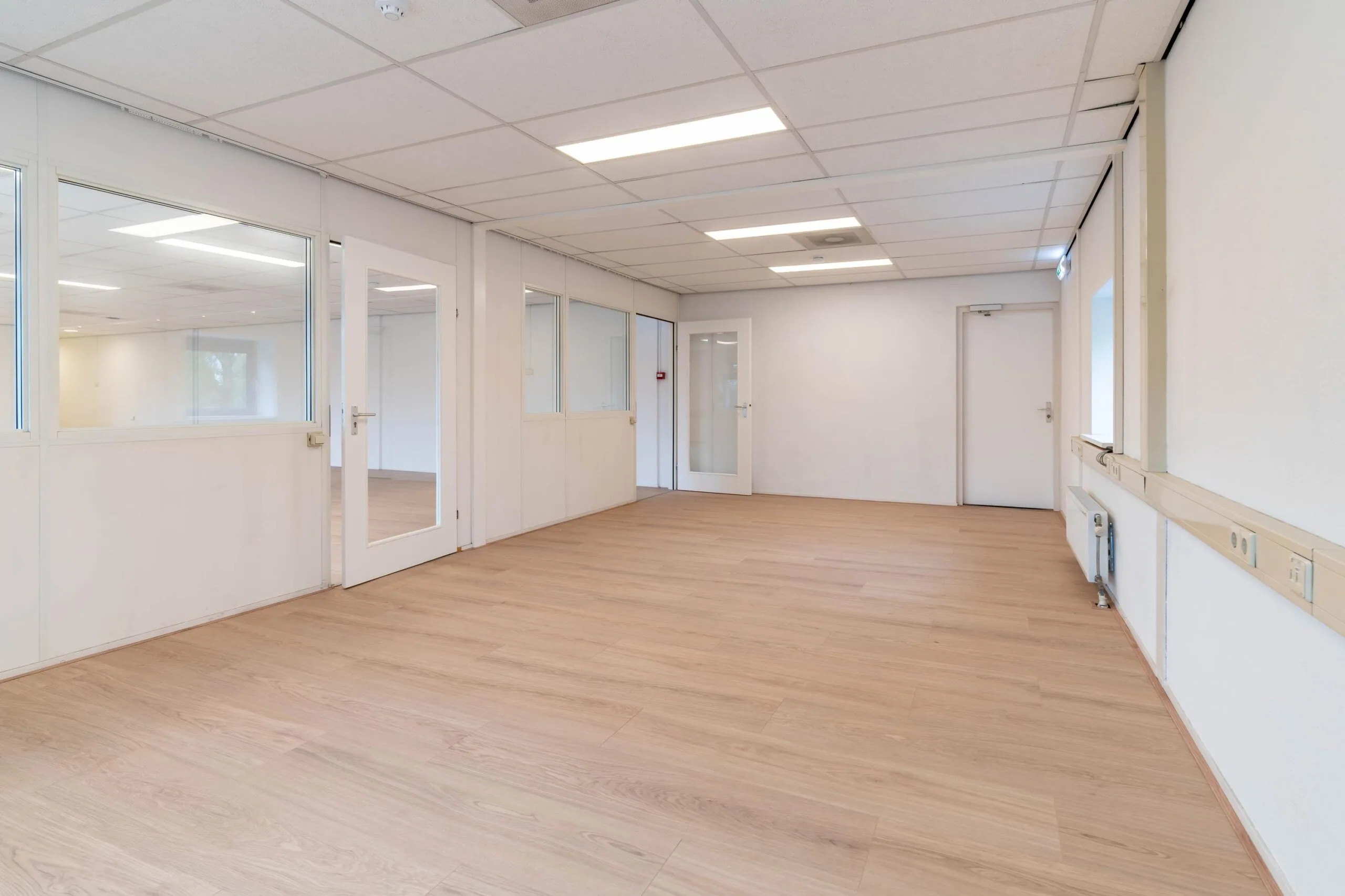 Leeg kantoorpand aan de Zuiderweg met lichte houten vloer, systeemplafond en glazen tussenwanden.
