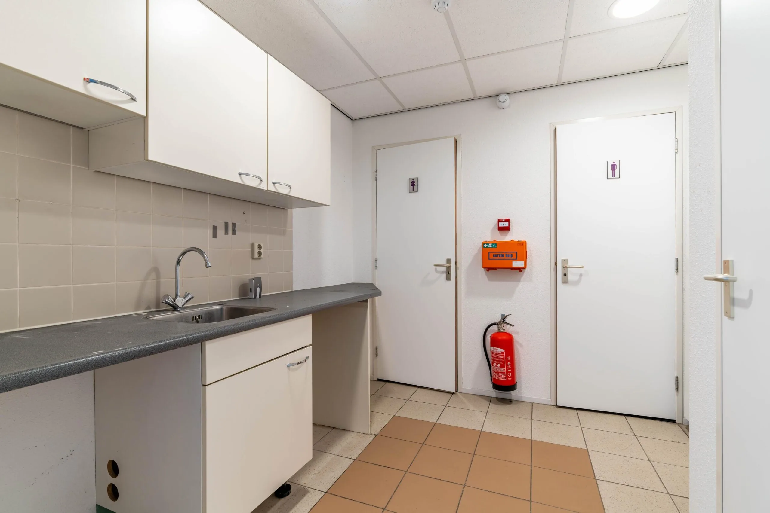 Kleine pantryruimte met spoelbak, bovenkasten en twee toiletruimtes in een zakelijke omgeving aan de Zuiderweg.