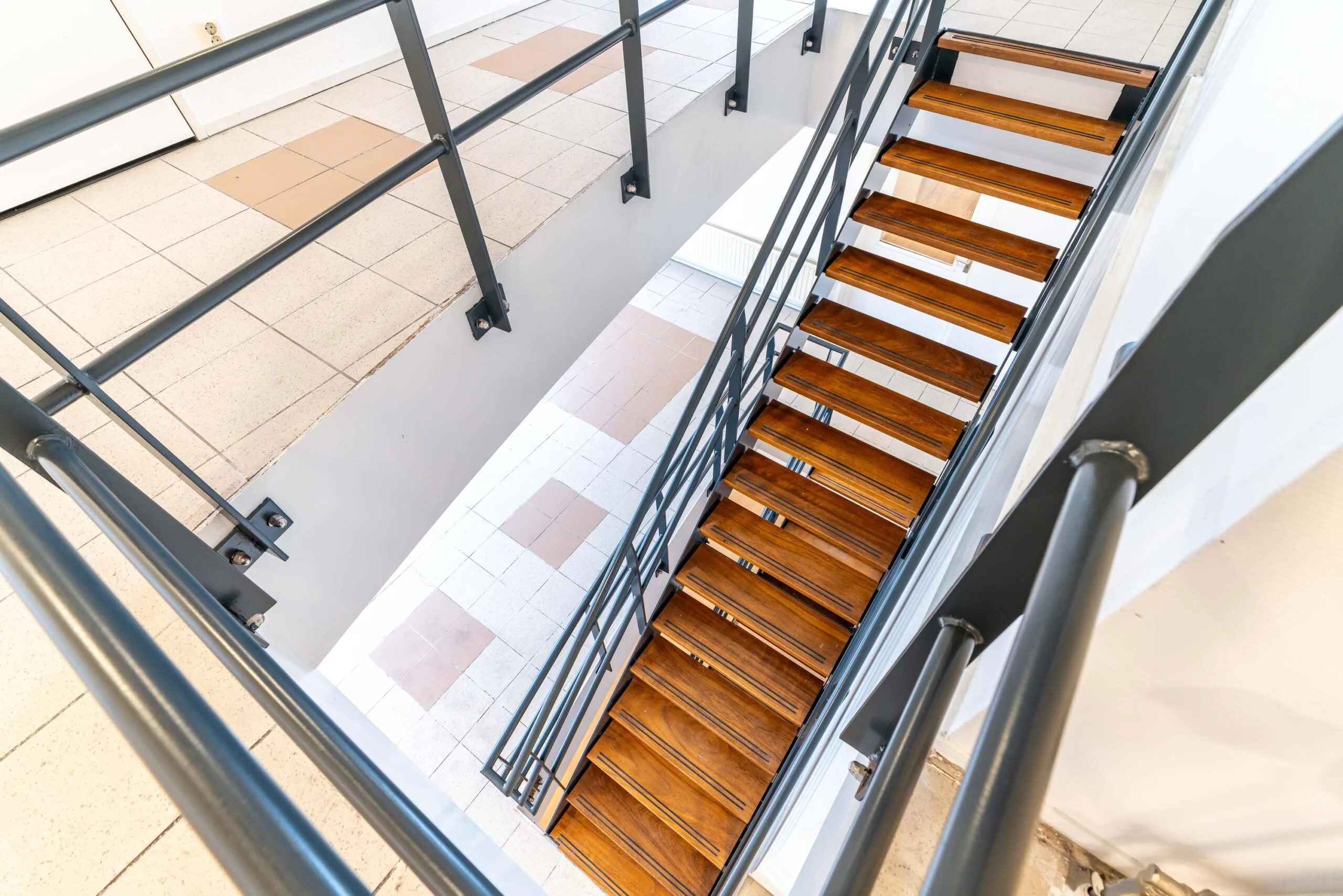 Houten trap met zwart metalen leuning in een licht trappenhuis aan de Zuiderweg.