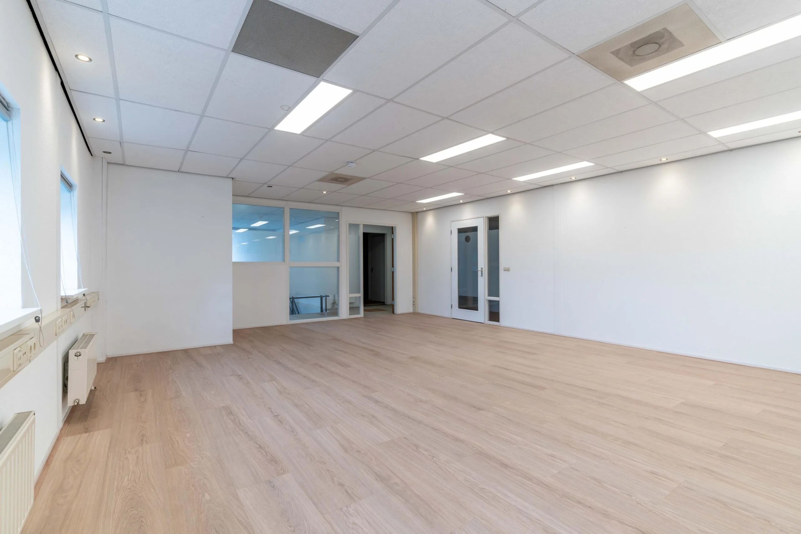 Lichte, lege kantoorruimte aan de Zuiderweg met houten vloer en systeemplafond.