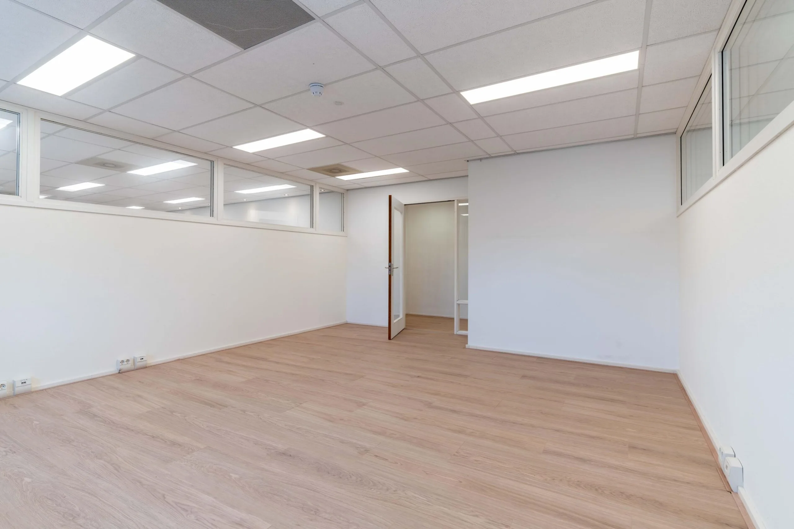 Leeg kantoor met lichte houten vloer, witte wanden en systeemplafond aan de Zuiderweg.