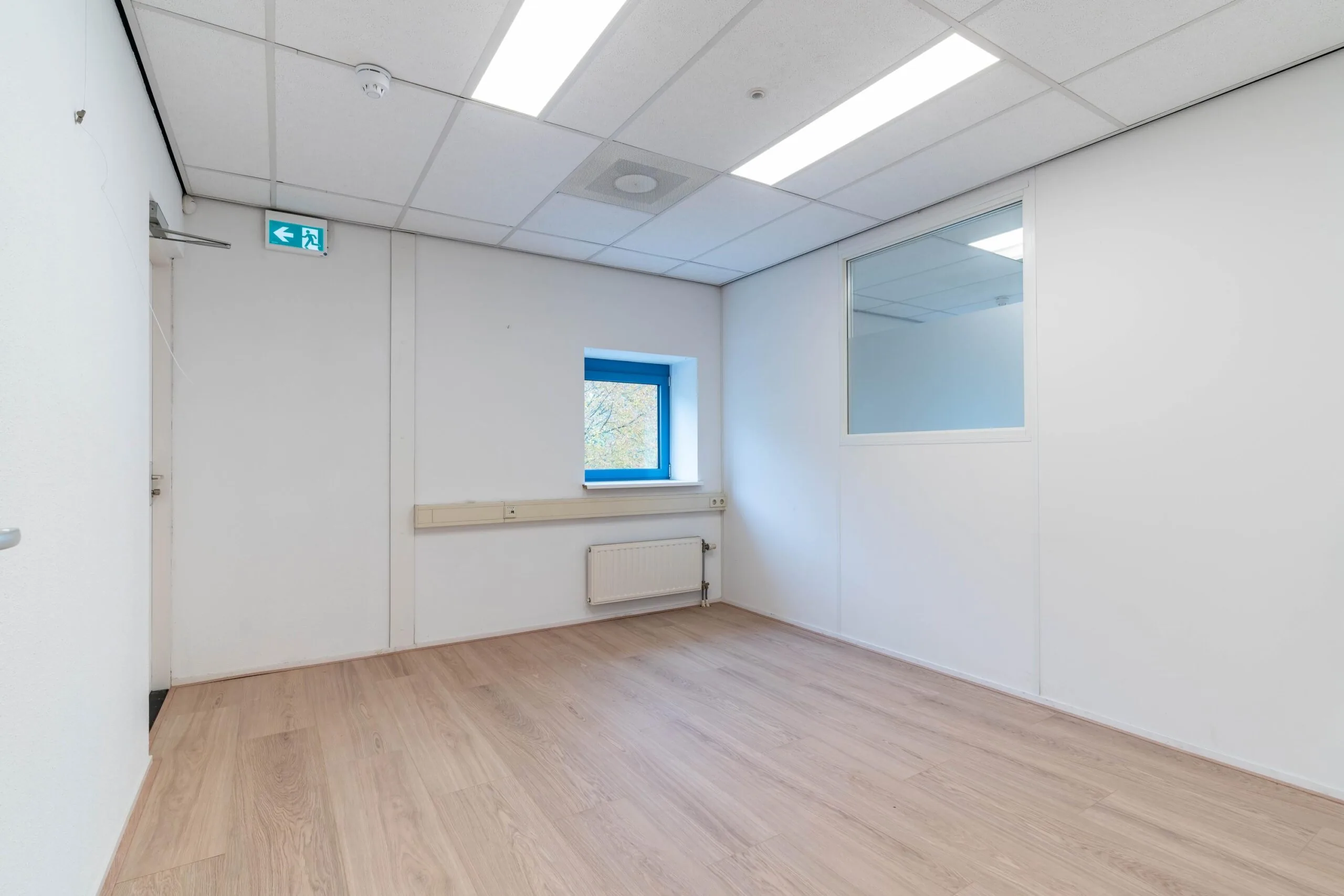 Lege kantoorruimte met laminaatvloer, systeemplafond, raam en glazen binnenwand aan de Zuiderweg.