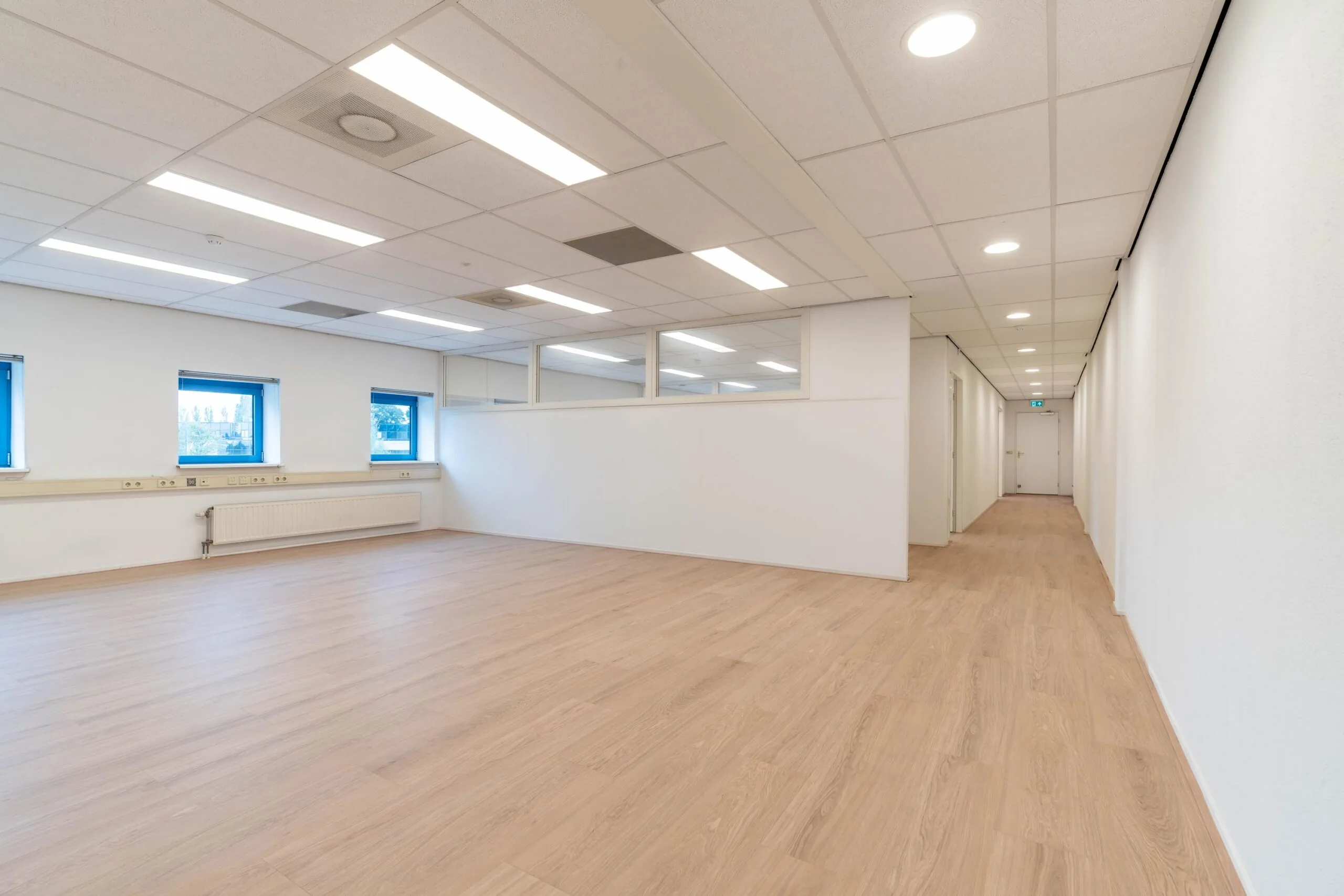 Lichte, lege kantoorruimte aan de Zuiderweg met houten vloer, systeemplafond en meerdere ramen.