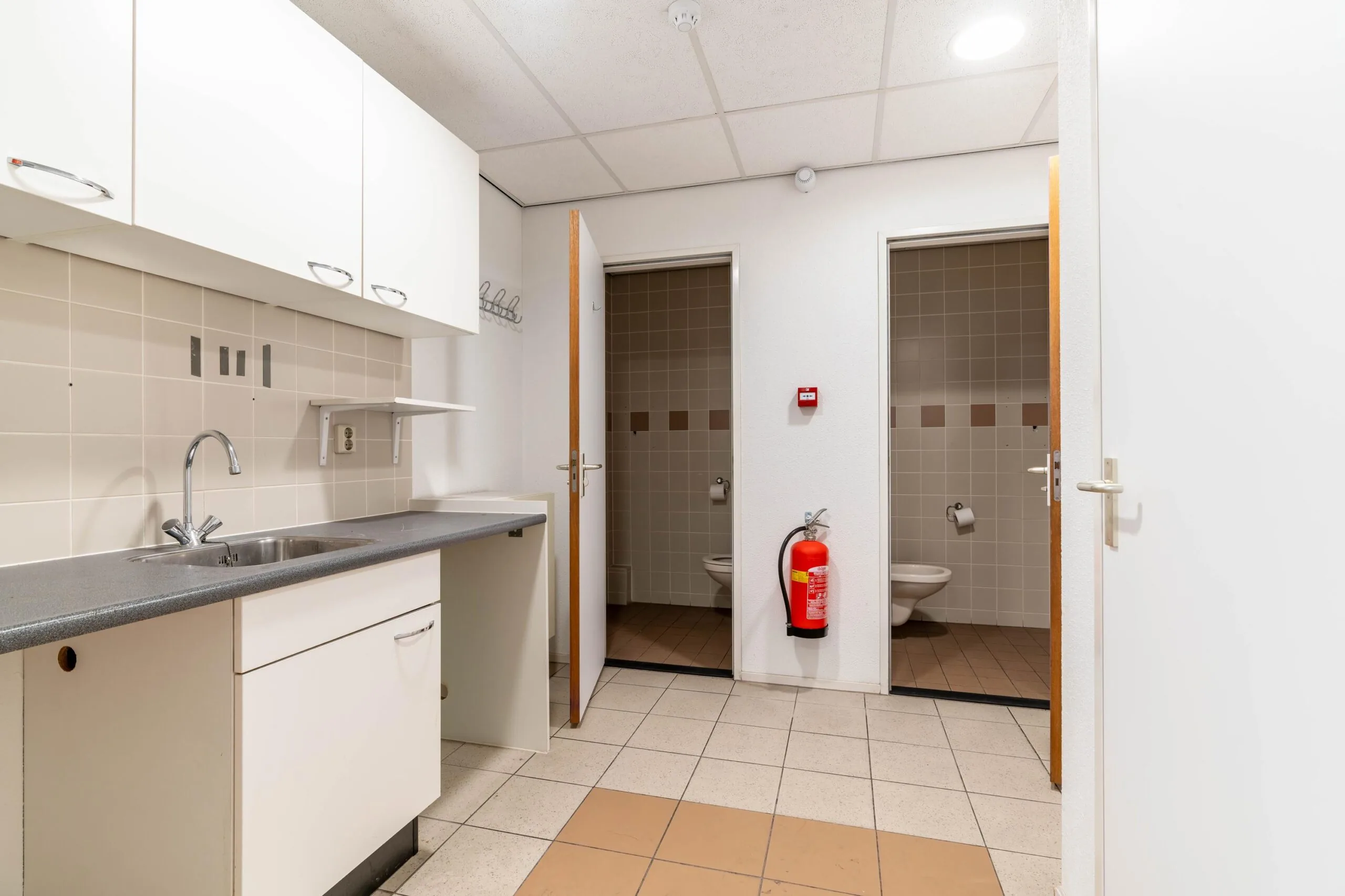 Keukenblok met spoelbak en bovenkasten in een gemeenschappelijke ruimte met twee toiletruimtes.
