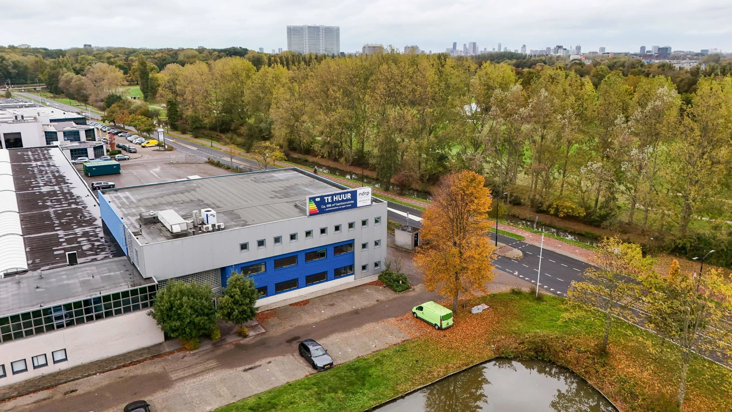 Bedrijfspand aan de Zuiderweg met 'Te Huur'-bord, gelegen naast een boomrijke weg en vijver.
