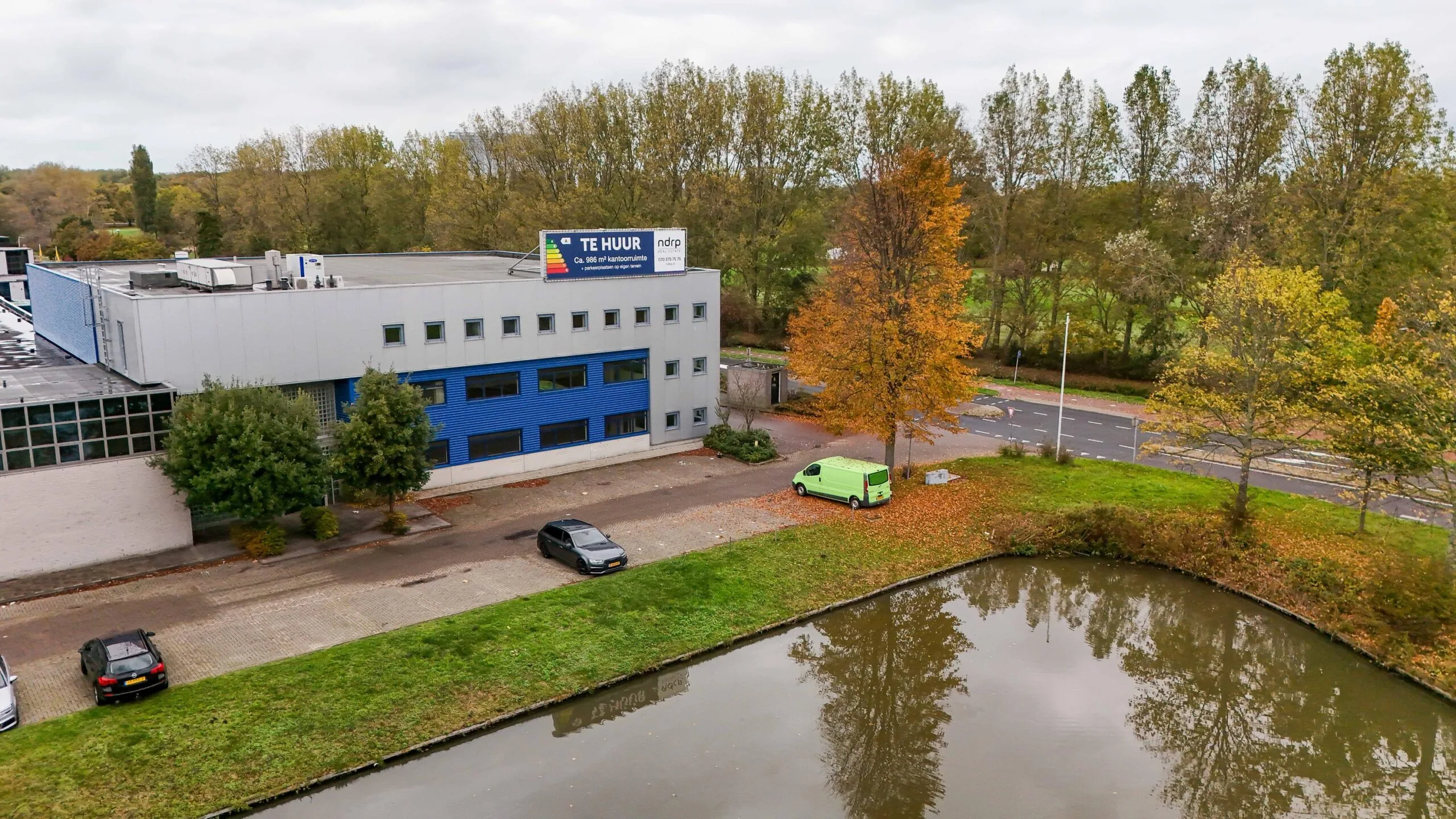 Kantoorpand aan de Zuiderweg met te huur-bord, gelegen naast een vijver en omringd door herfstbomen.