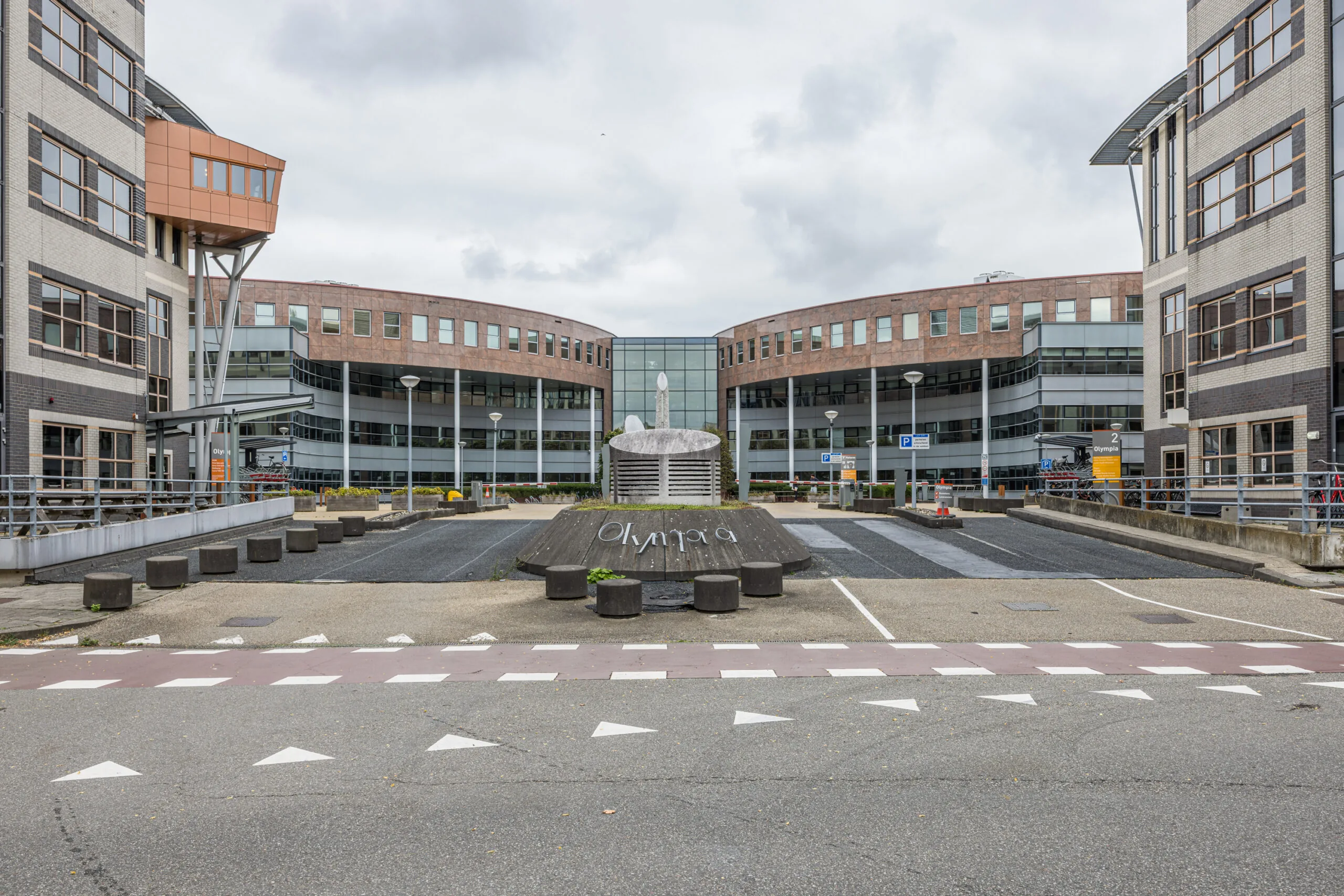 Modern office building complex named "Olympia" with a central sculpture and roundabout in front.