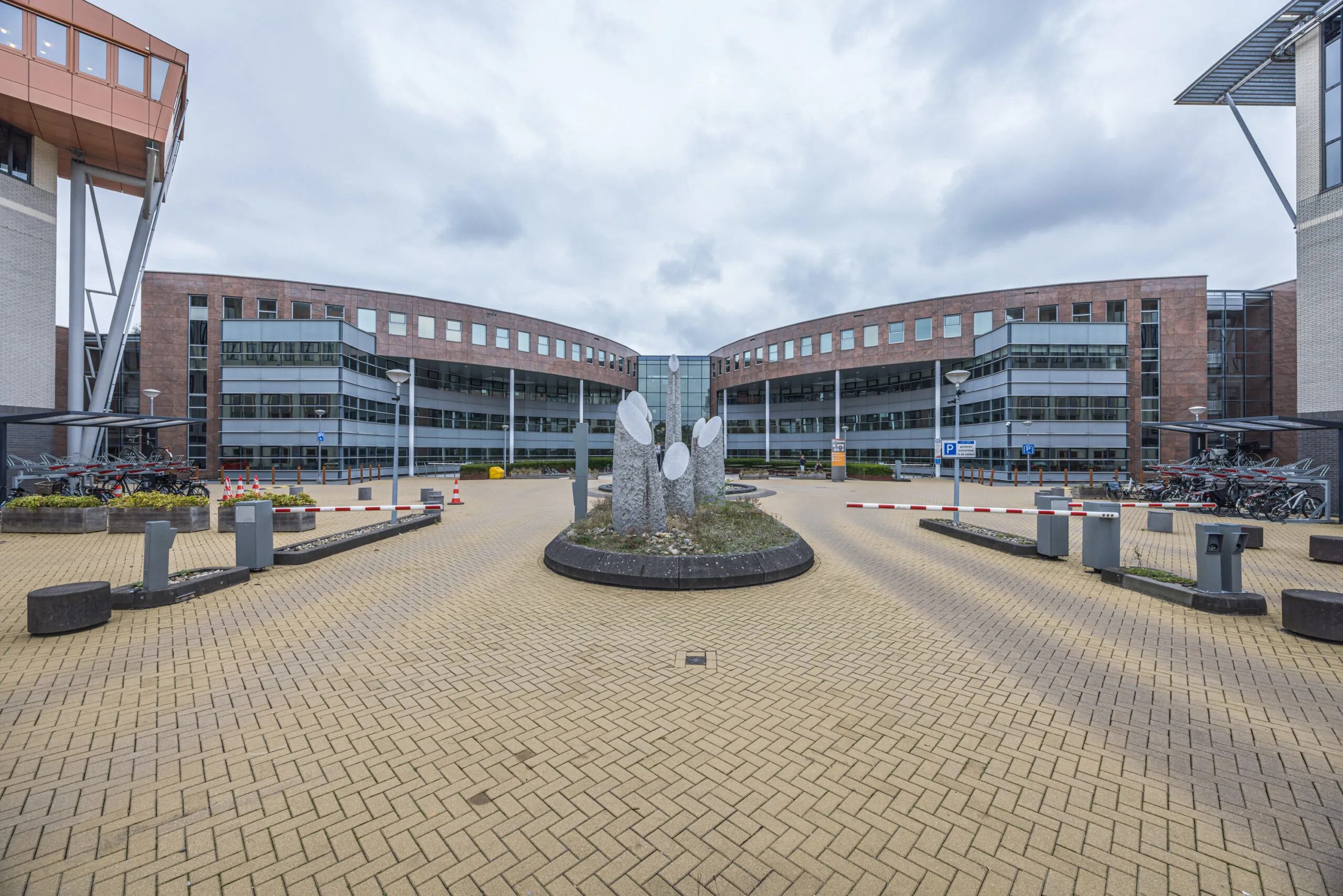 Modern office building of Olympia with a central stone sculpture and bicycle parking in front.
