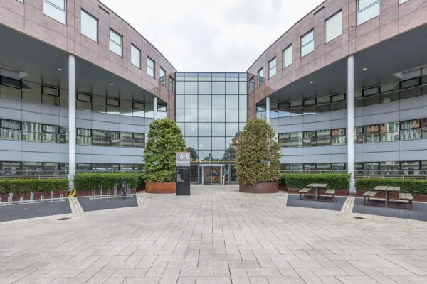 Modern office building entrance at Olympia 6-8 with large glass façade and surrounding landscaping.