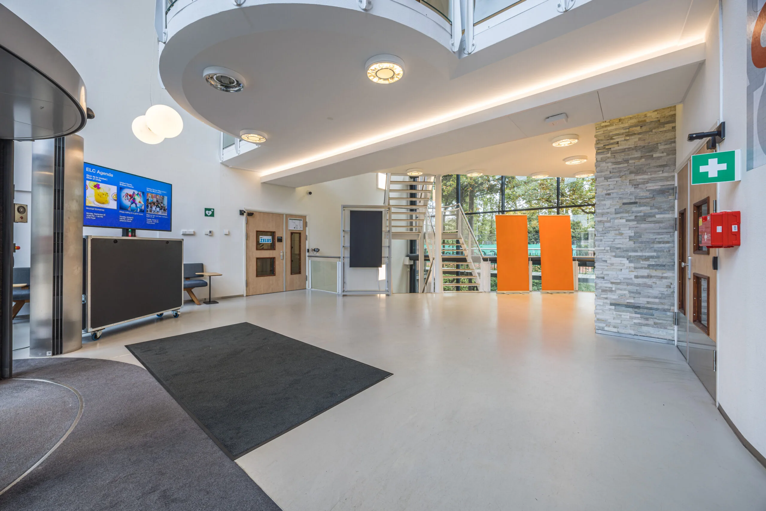 Modern entrance hall of the Olympia building with a spiral staircase, digital signage, and large windows.